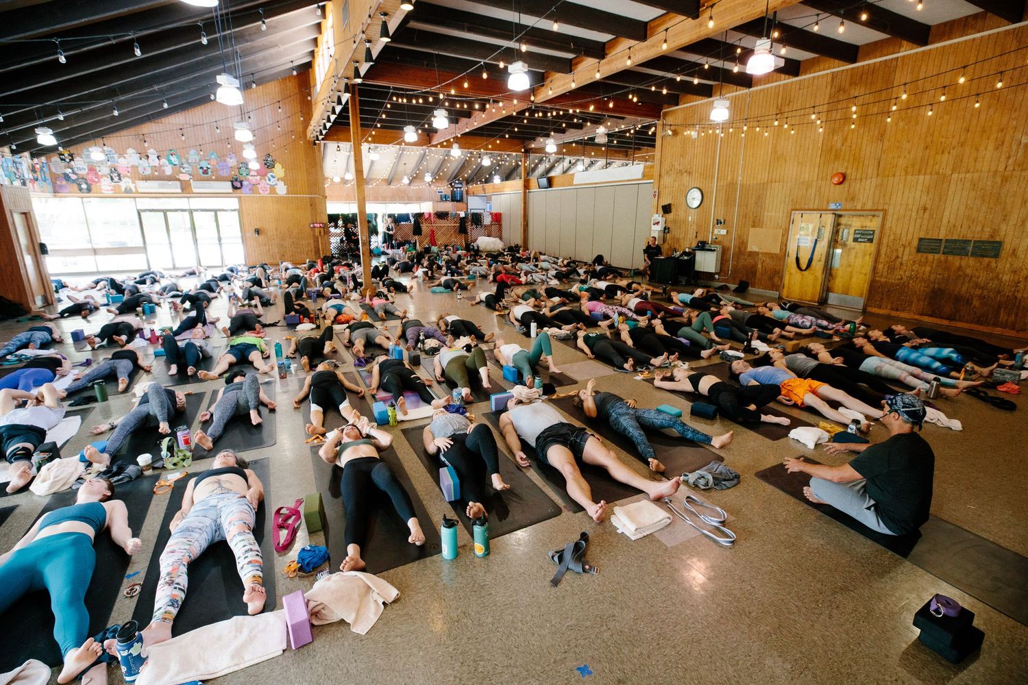 A wide-angle view of a large group meditation session in a string-lit indoor space.