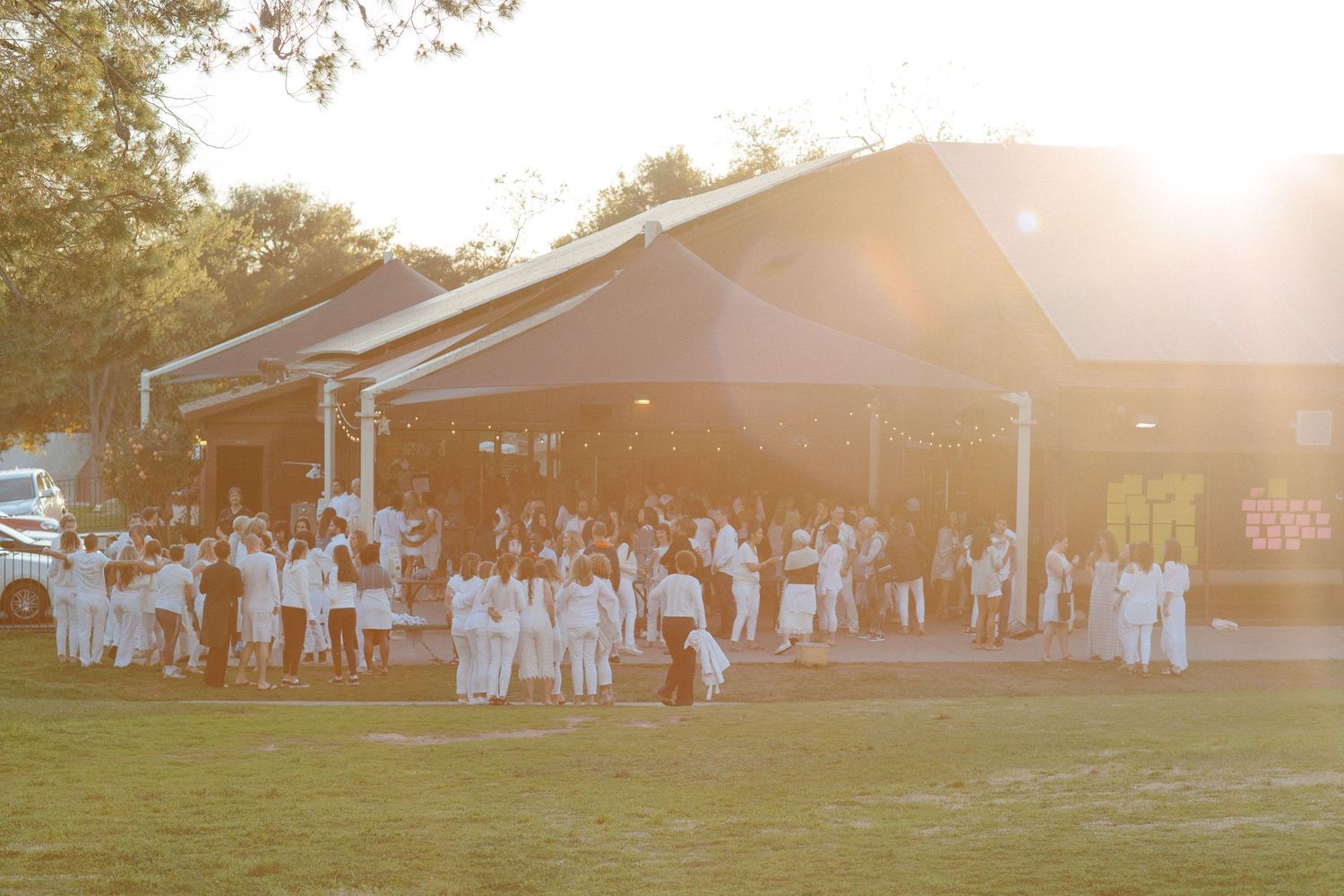 A large crowd gathers outside a pavilion during sunset.