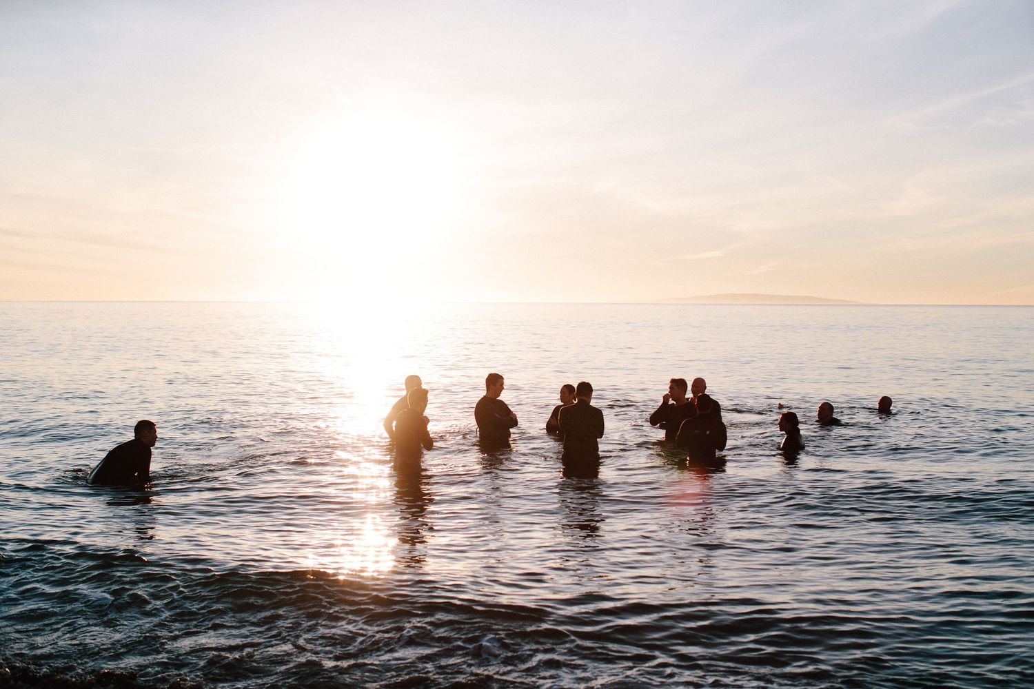 Silhouettes of people in water against a sunset ocean backdrop.