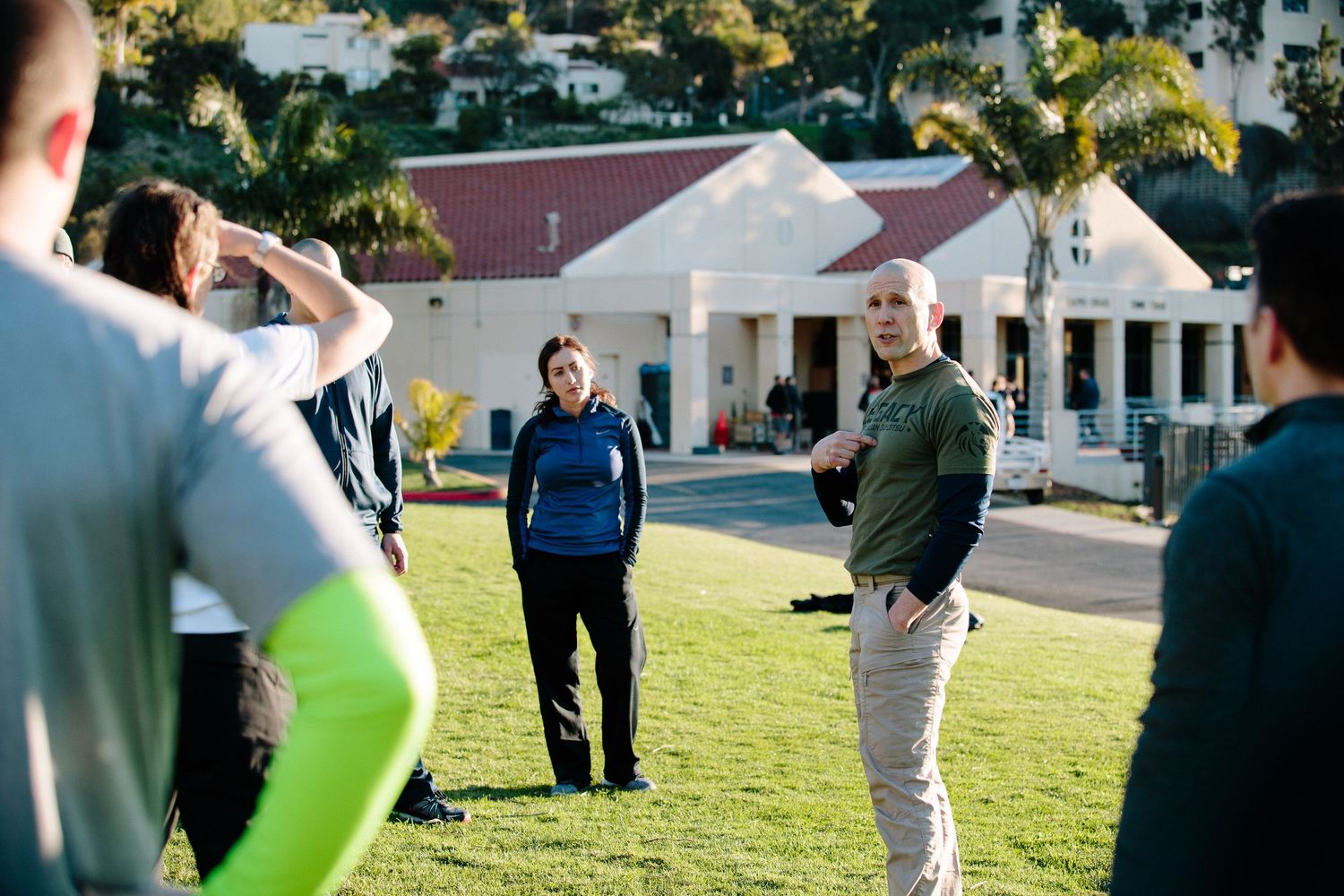 People gathered outdoors for a training session on a sunny day with white buildings in background.