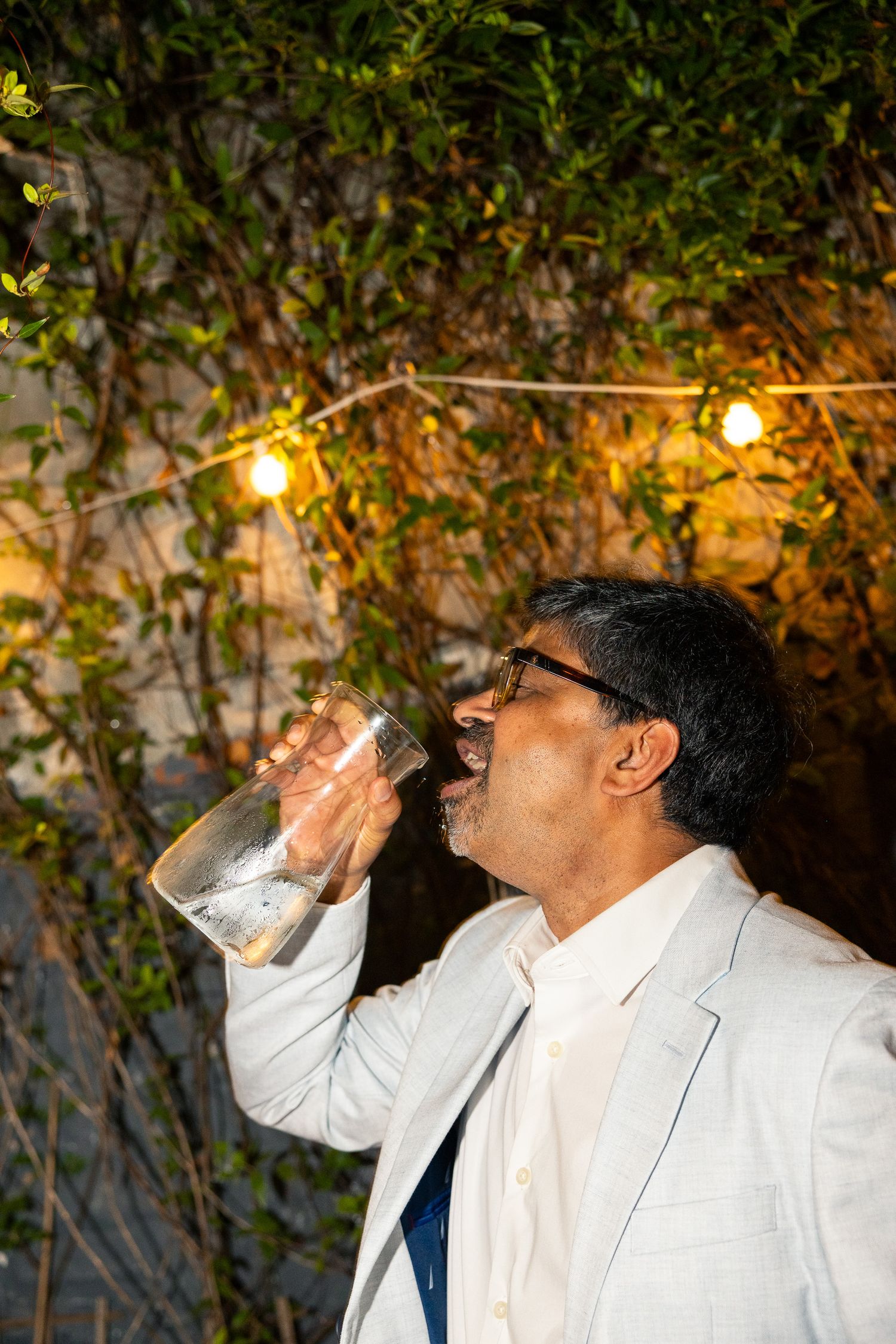 A person in a white blazer takes a celebratory drink during an outdoor party.