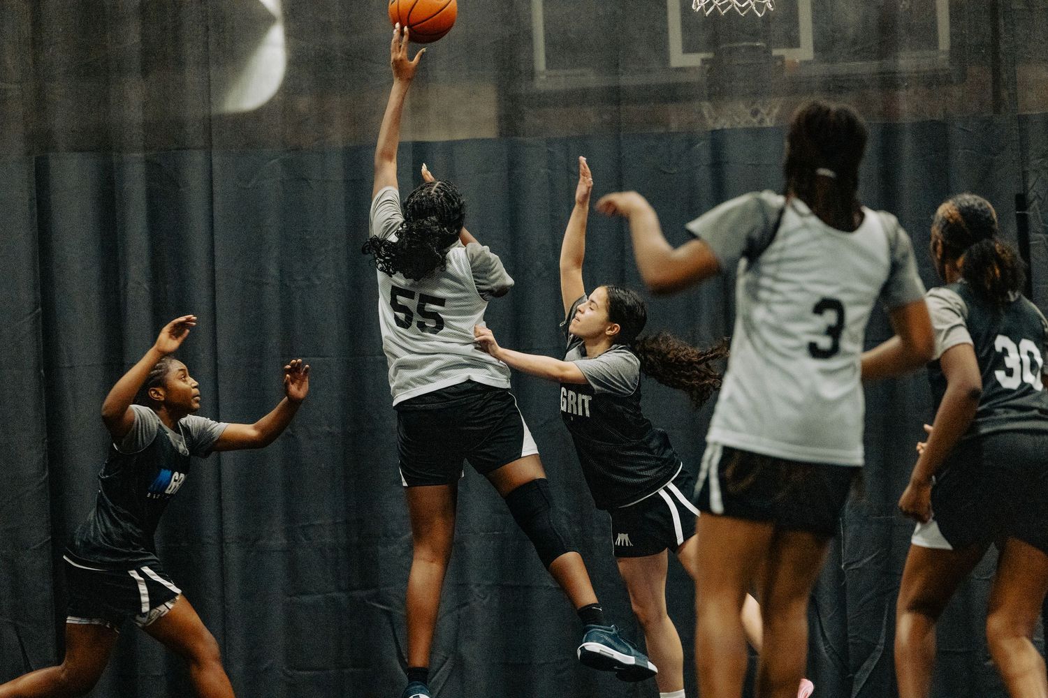 Players in black and white uniforms chase after a basketball on an indoor court during a game.