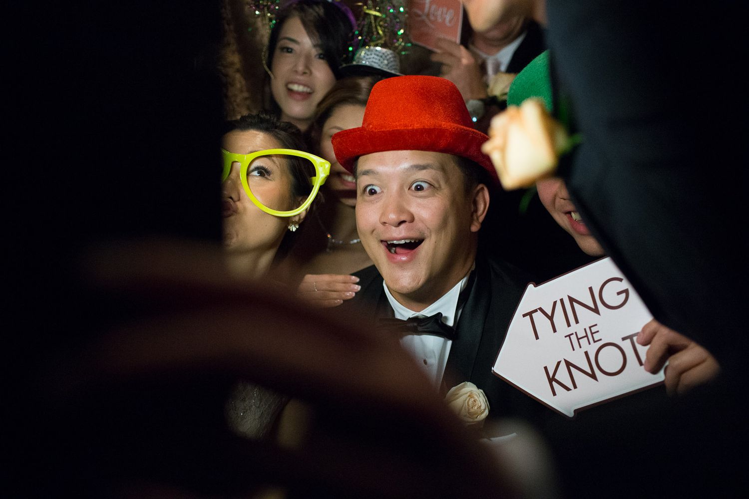 A guest in a red hat holds a 'Tying the Knot' sign in a photo booth.
