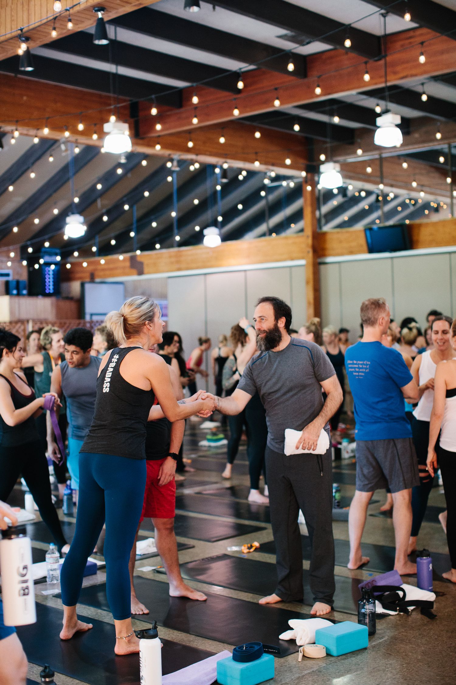 People mingling in an industrial-style fitness space decorated with string lights and exposed beams.
