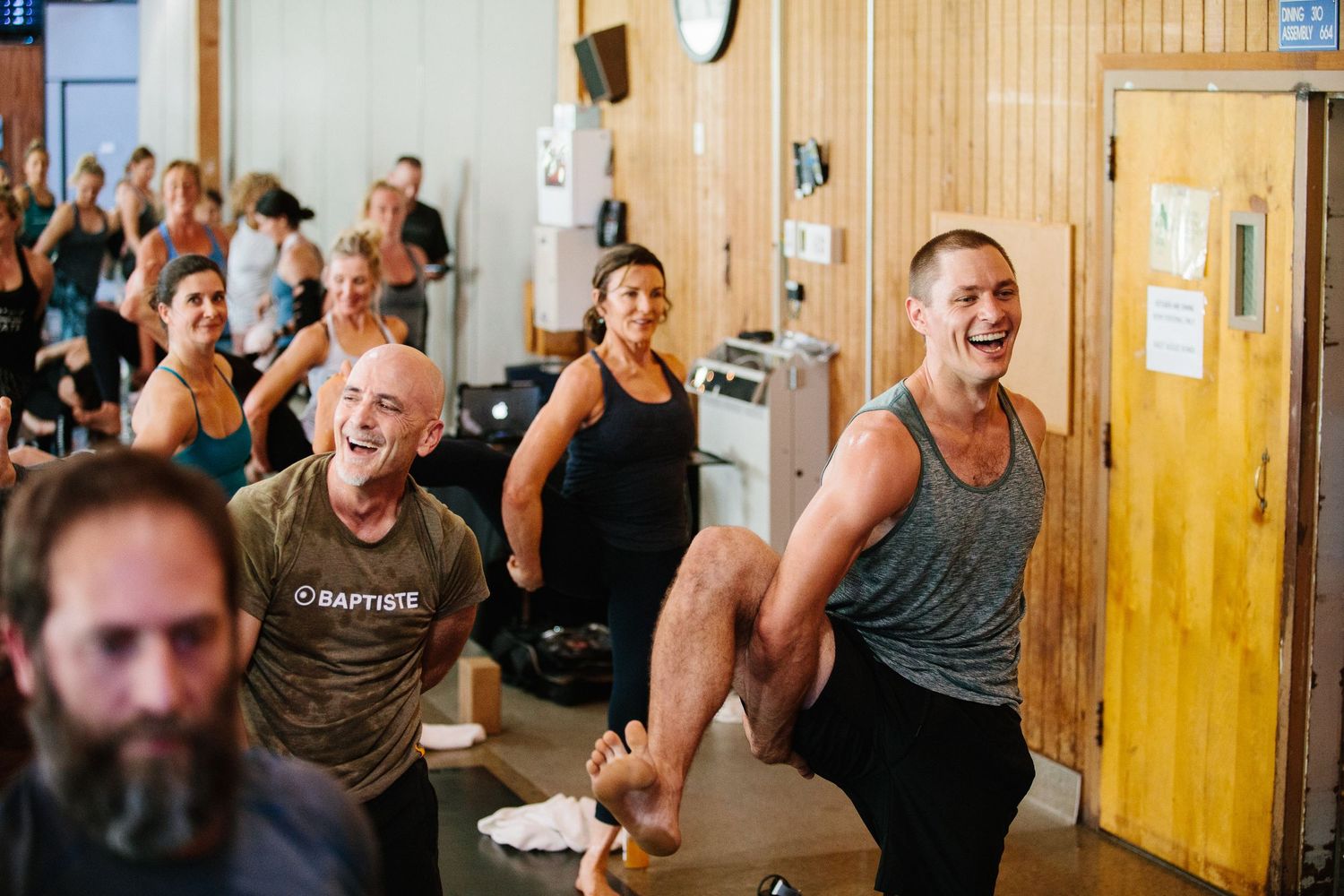 A crowded fitness class with people doing exercises together in a wooden-paneled health studio.
