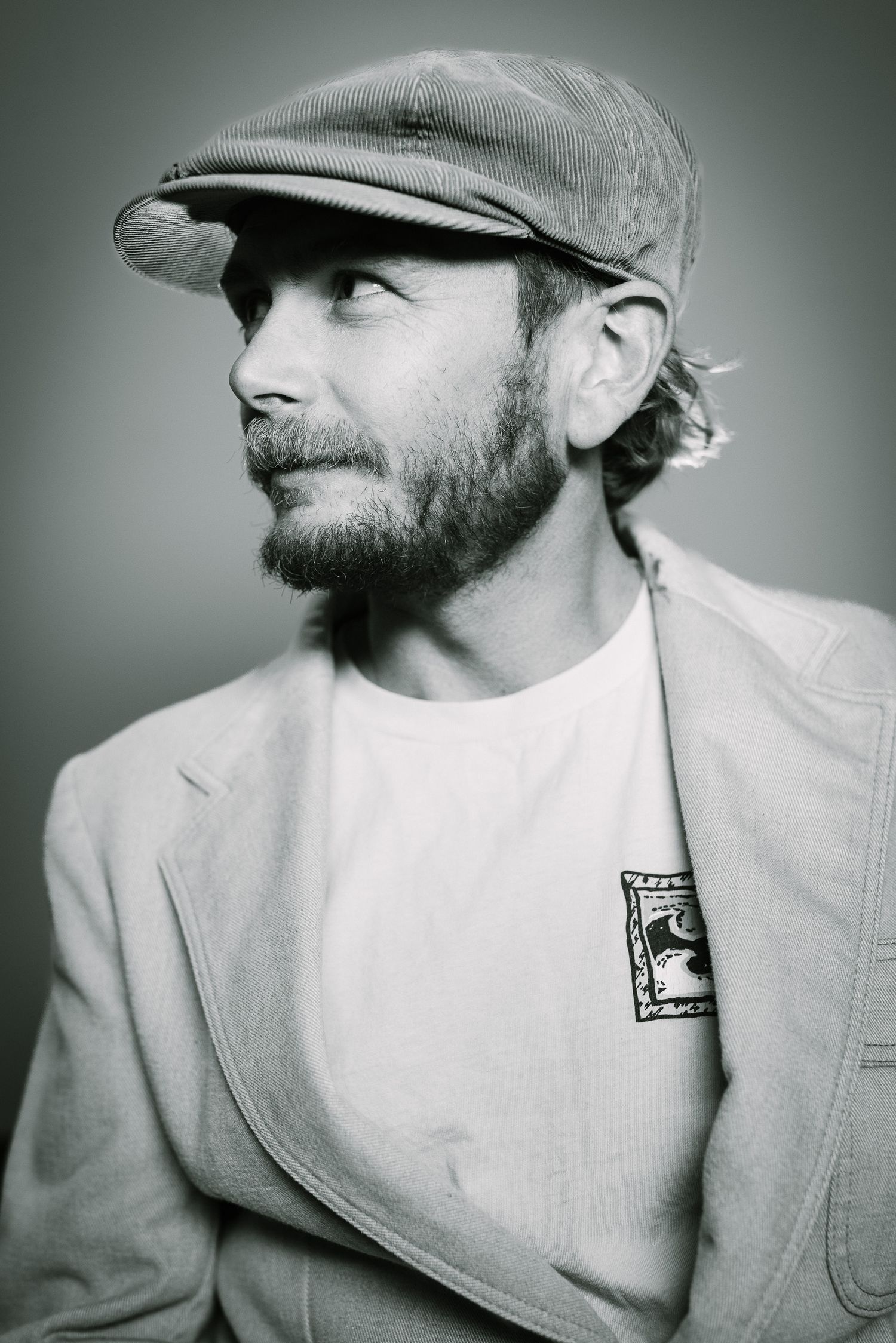 Profile portrait of person in flat cap and blazer looking to the side with natural lighting.
