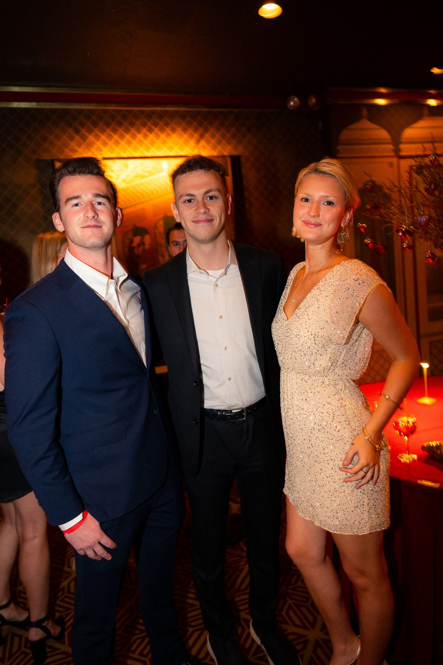 Three people in formal attire pose together at an elegant evening event.