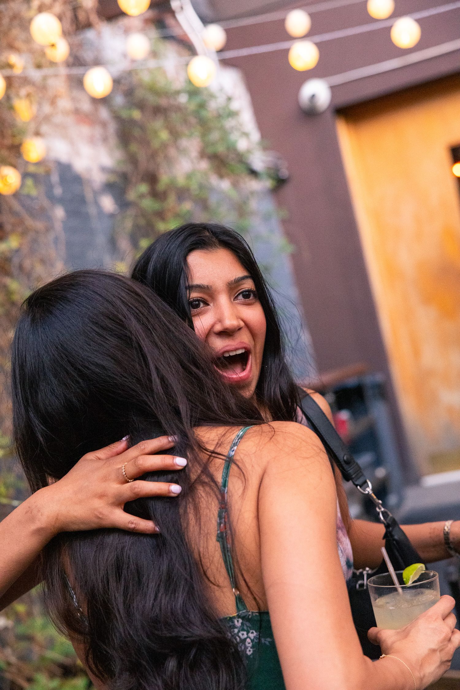 An excited hug shared between friends at an outdoor party with string lights.