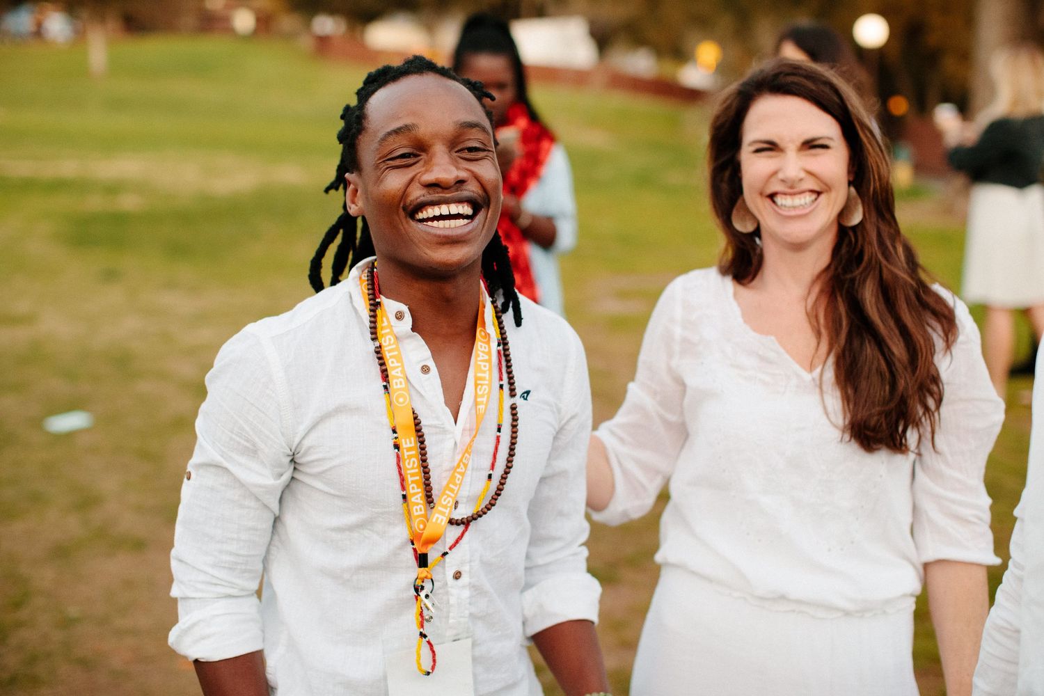 People wearing white clothing gather outdoors on grass during a sunny day event.