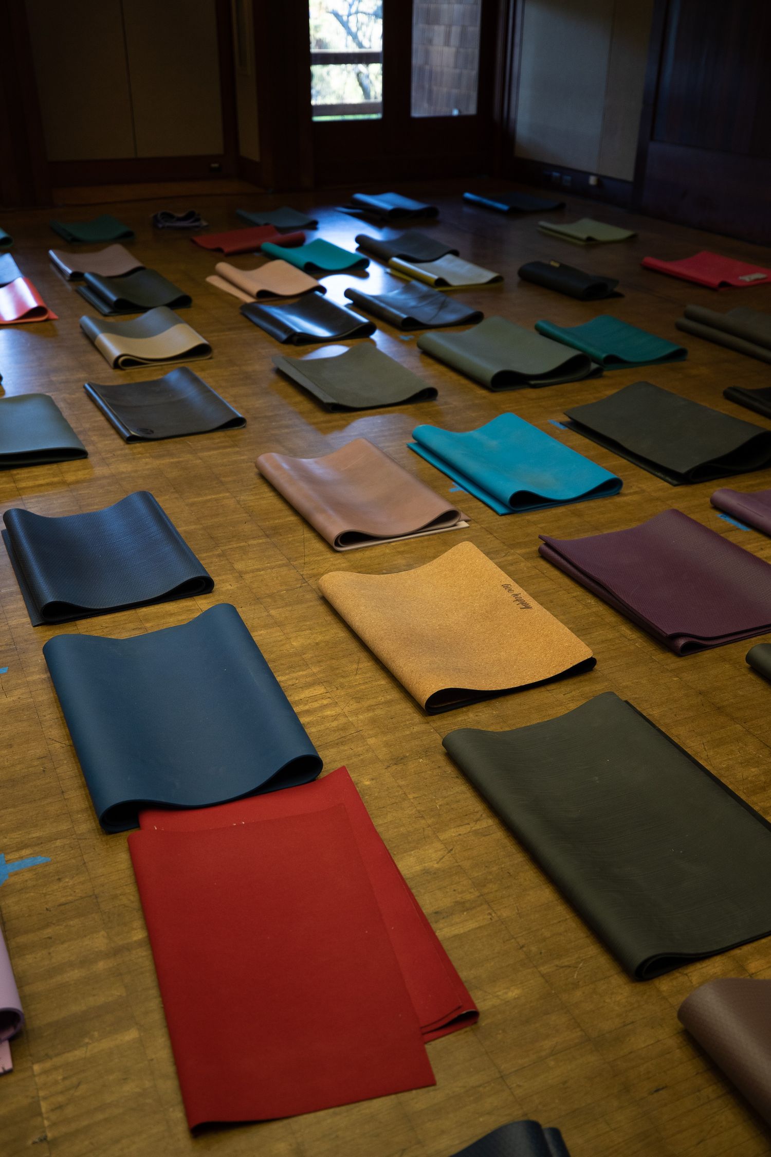 Colorful yoga mats laid out in rows on a wooden floor in a studio setting.