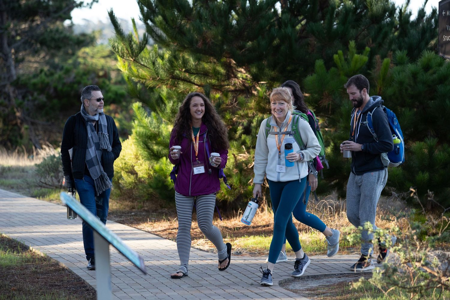 Group of people walking together outdoors on a path through green foliage on a sunny day.