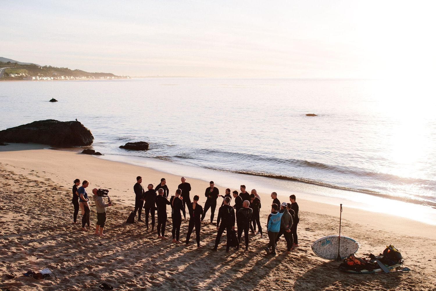 A group of people stand silhouetted on a beach at sunset.