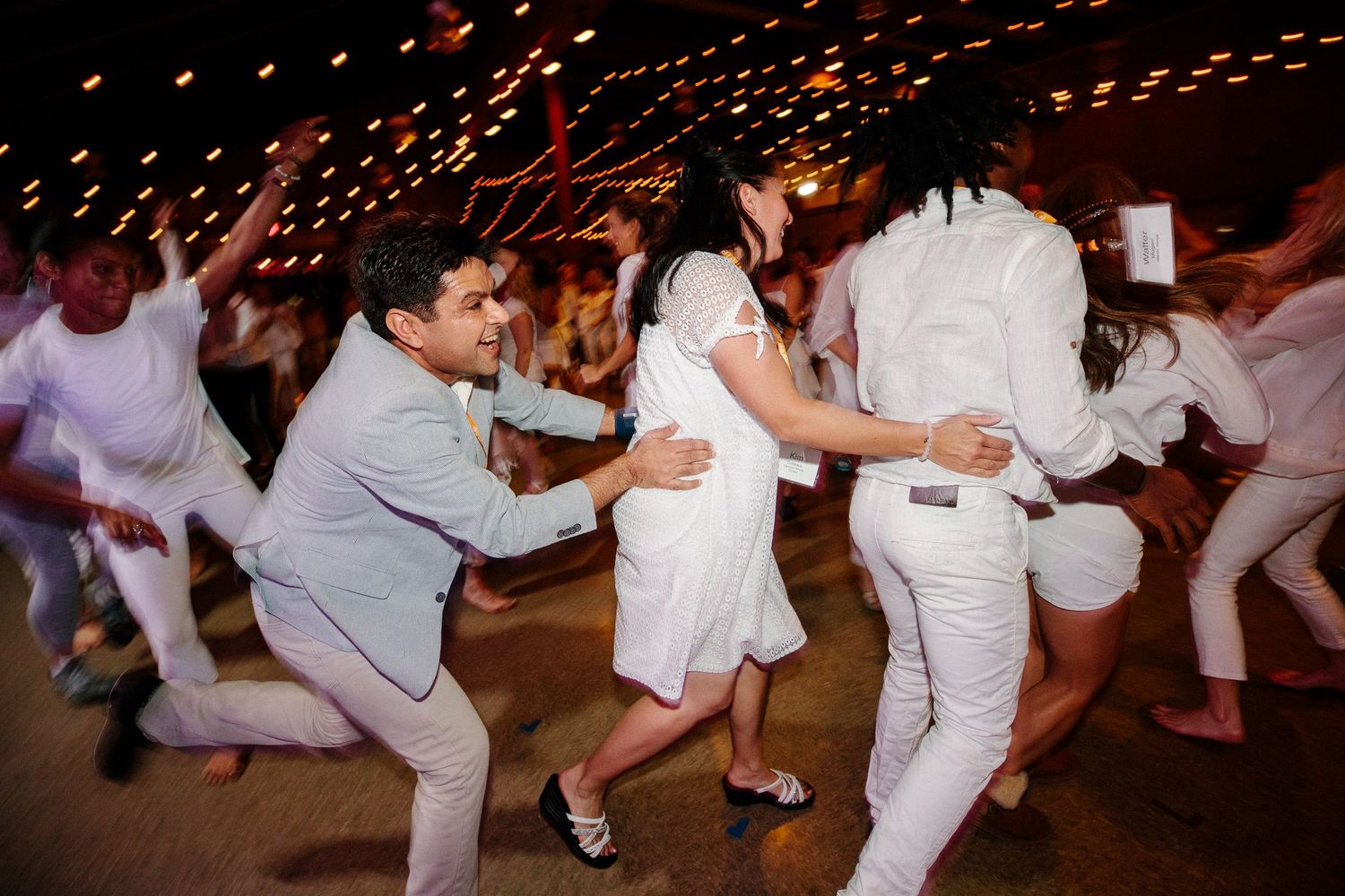 Group of people in white clothing performing dance or exercise movements.