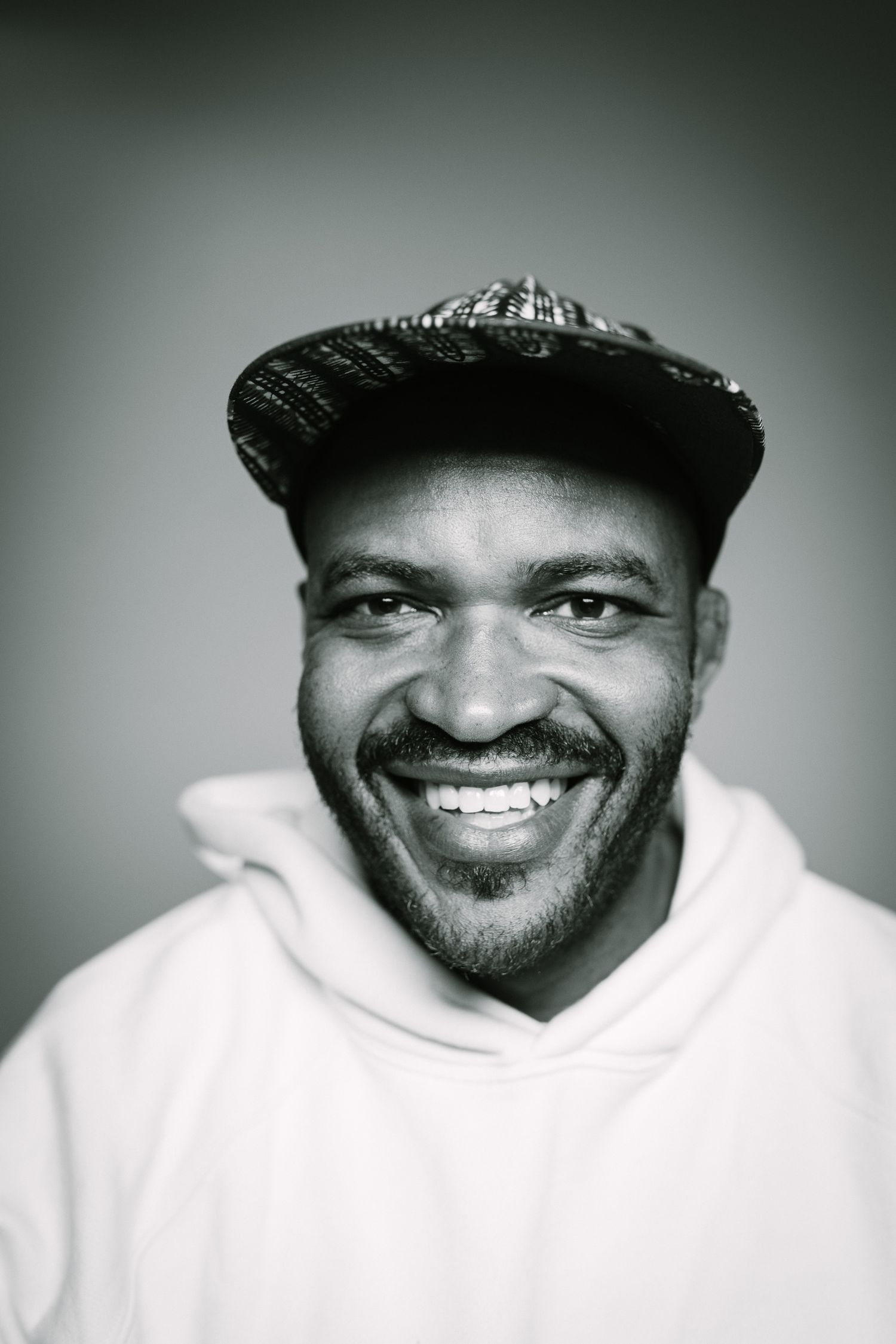 Black and white portrait showing bright smile, baseball cap and white hoodie.