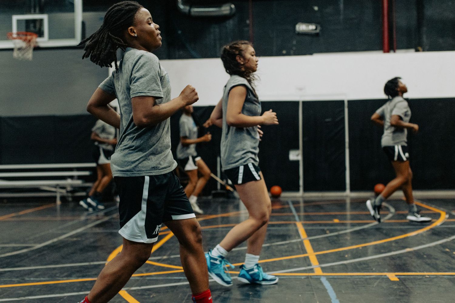 Athletes performing agility drills and running exercises in a black and gray indoor sports facility.