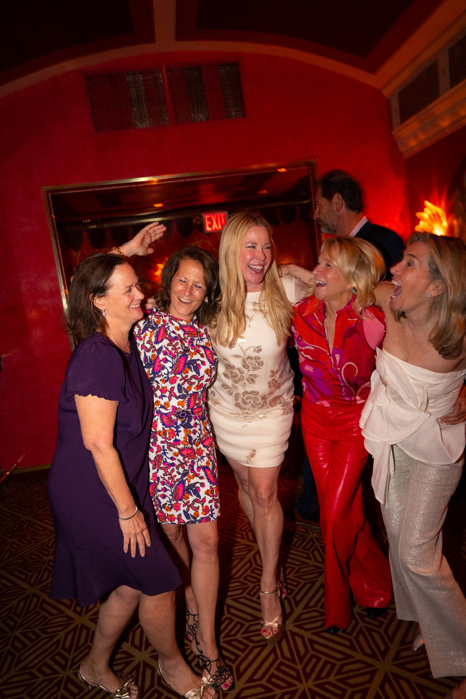 Friends laughing together against a red wall at a party venue.