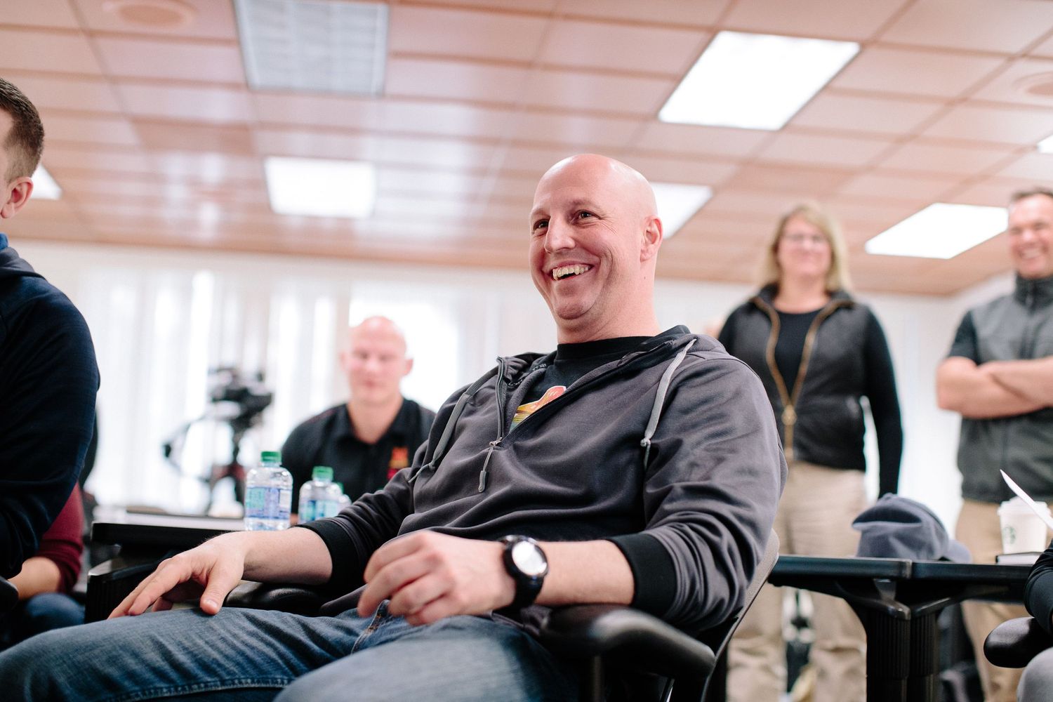 A group of people laughing and smiling during a casual meeting in a bright office space.