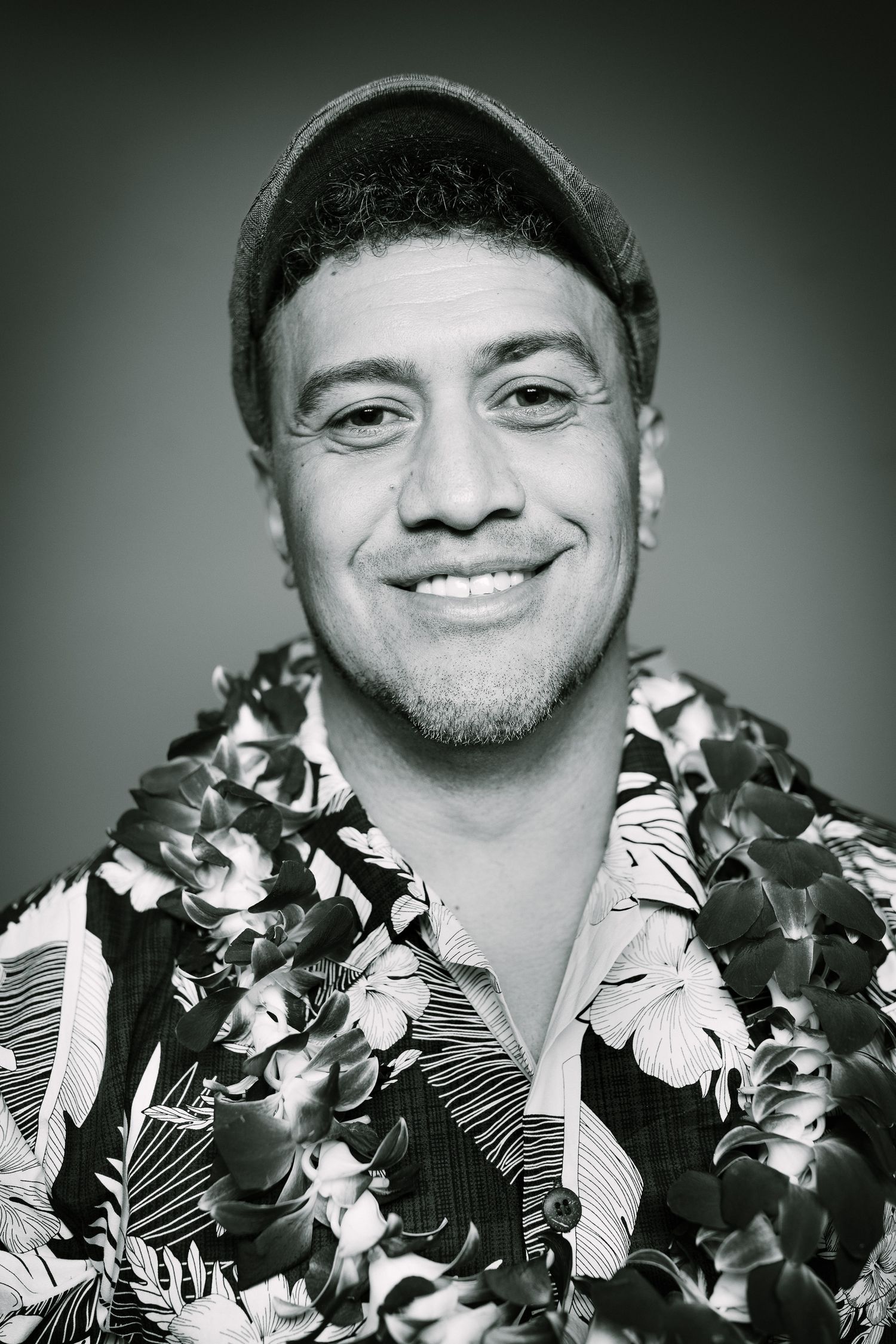 Black and white portrait of a person wearing a floral Hawaiian shirt and beanie smiling at the camera.
