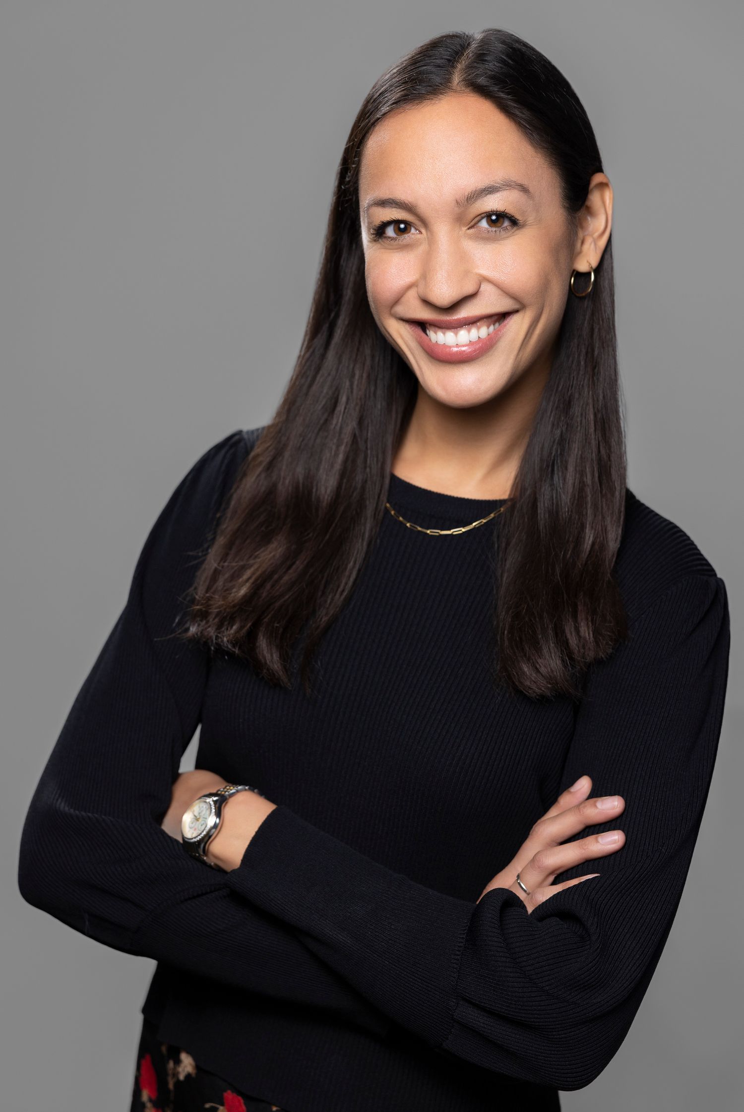 Professional portrait of a person in a black sweater with crossed arms and long dark hair.