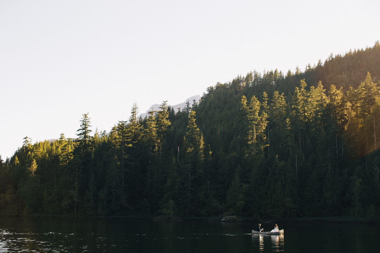 A serene lake reflects evergreen forests as a small boat floats in the distance.