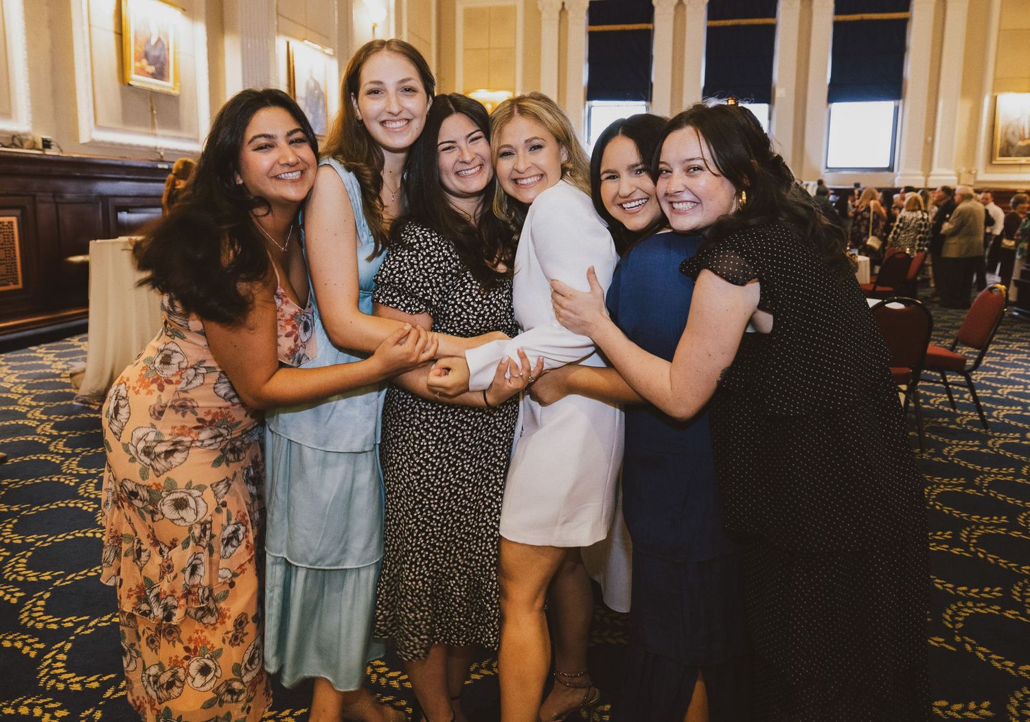 A group of friends embrace in a joyful moment at a formal event.
