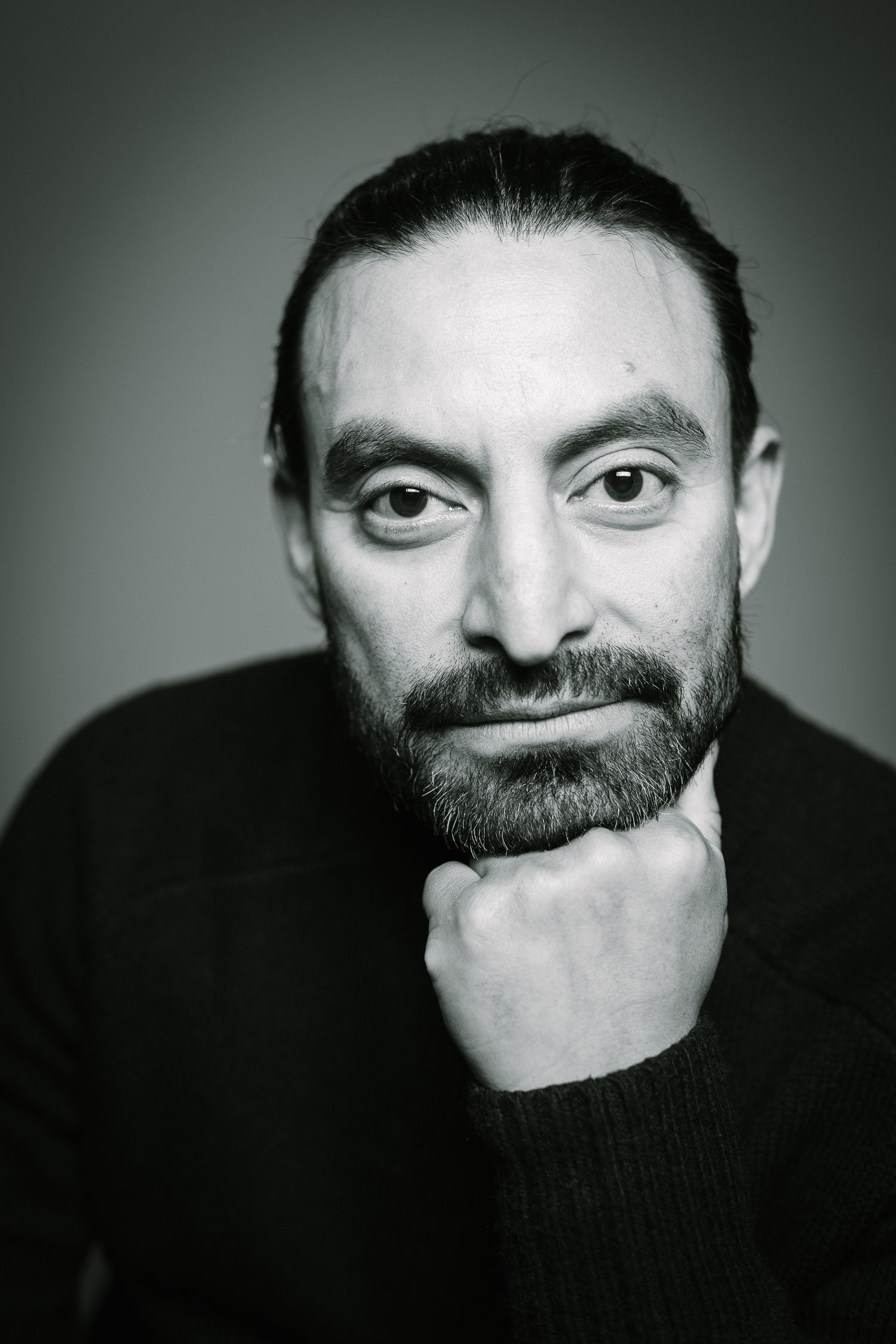 Dramatic black and white portrait of thoughtful person in dark sweater with hand under chin.
