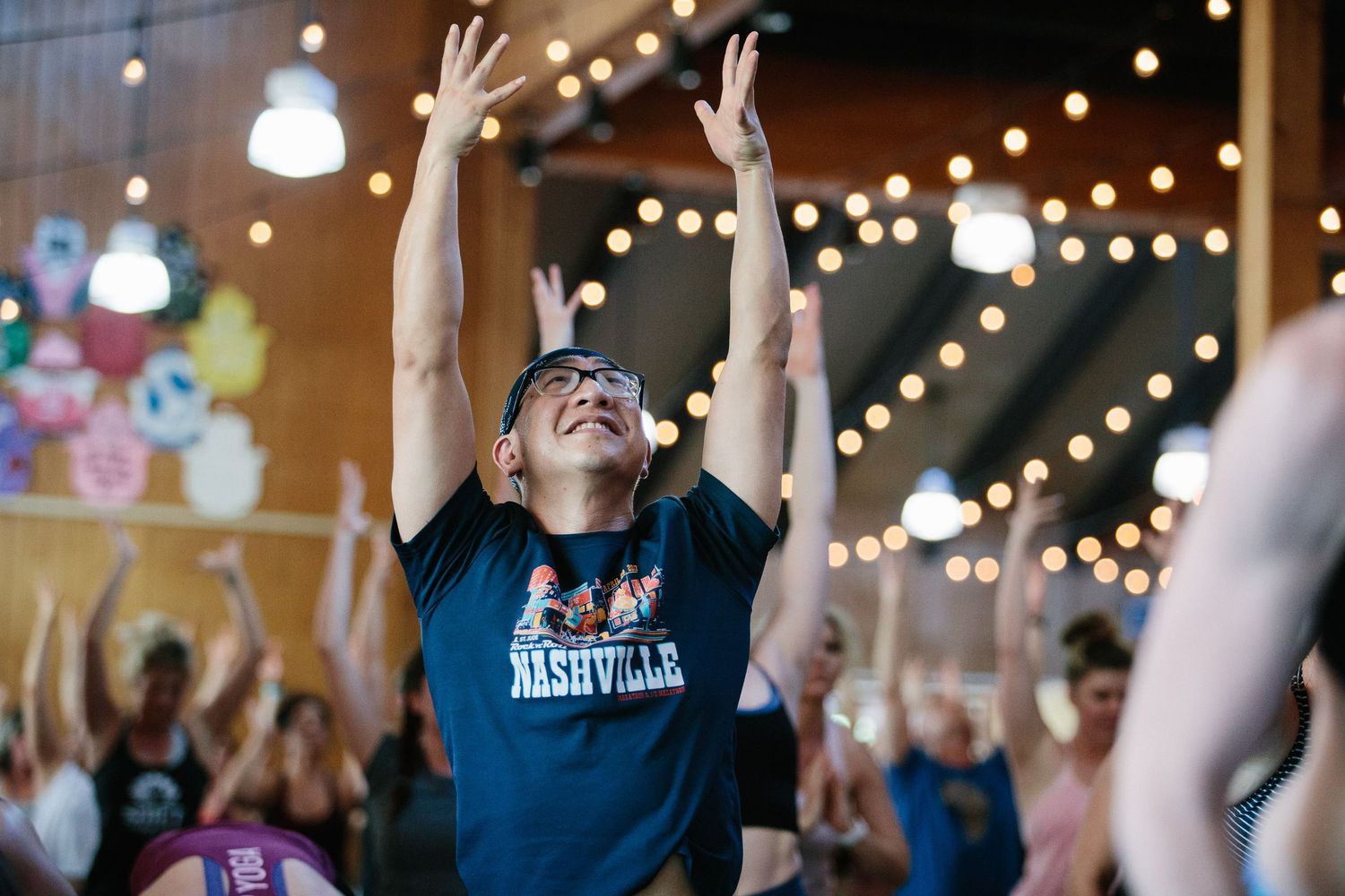 A person wearing a Nashville shirt raises their arms in celebration during an indoor event.
