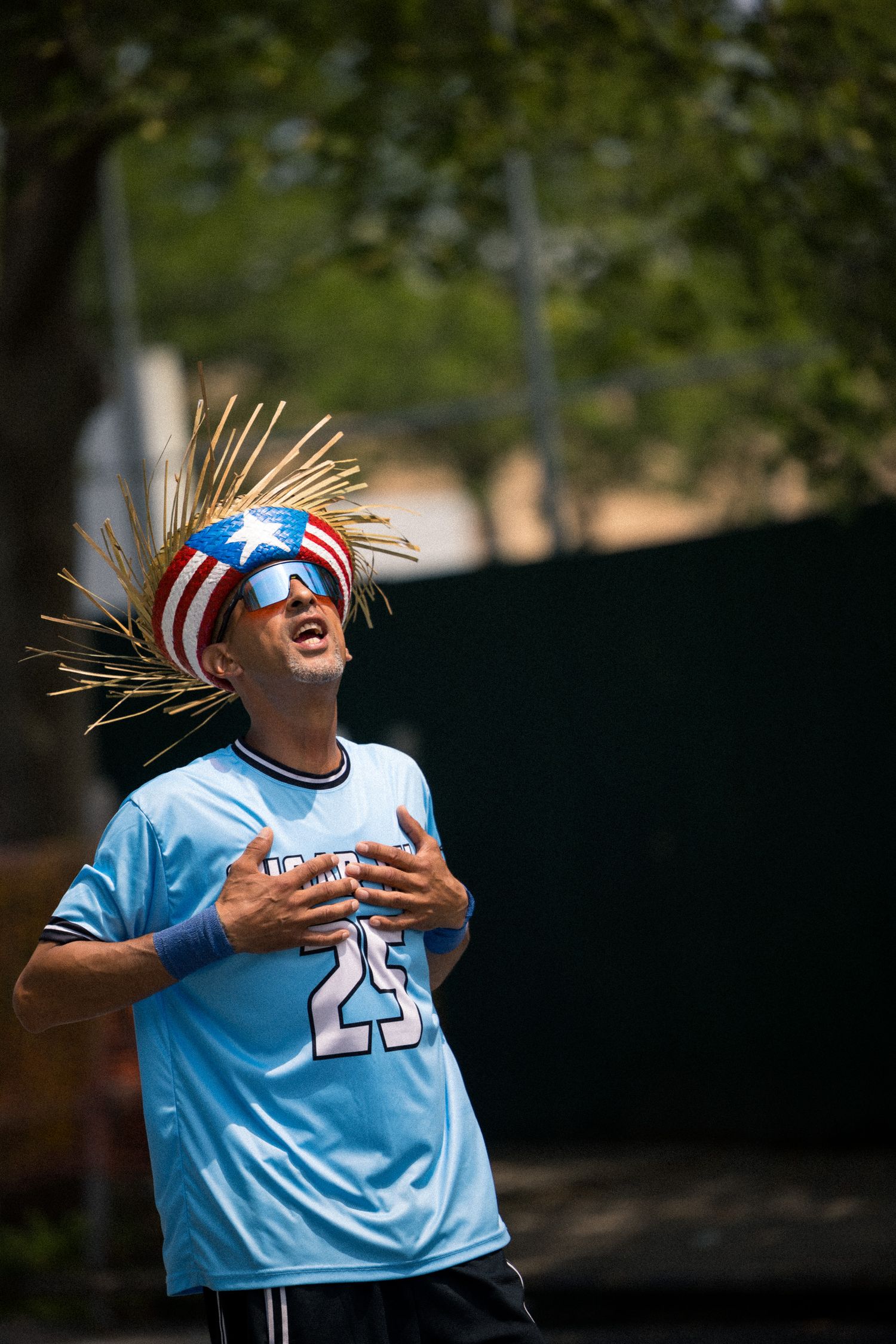 Baseball player in light blue jersey reacting enthusiastically while wearing sunglasses and American flag bandana.