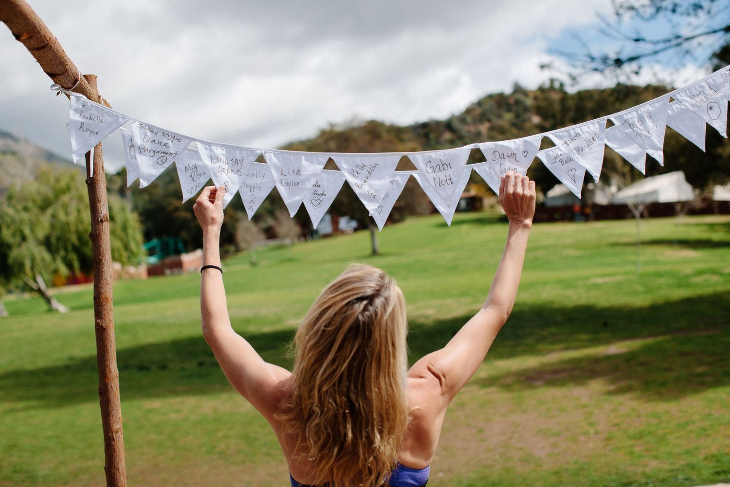 Person reaching up to white triangle banner flags against cloudy sky and green landscape.