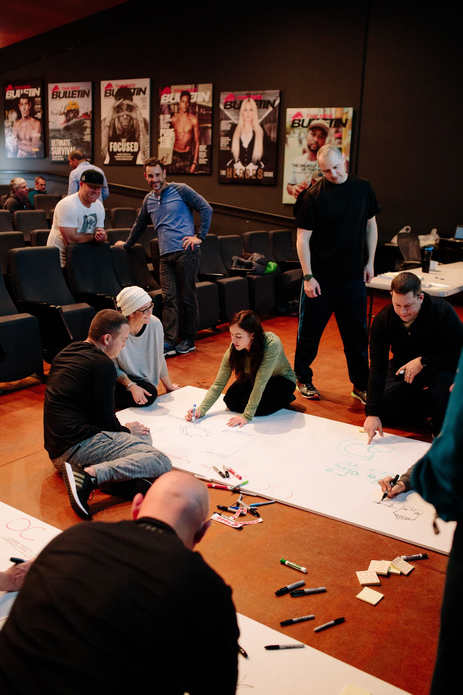 Group planning session with people gathered around papers on floor with movie posters on wall.
