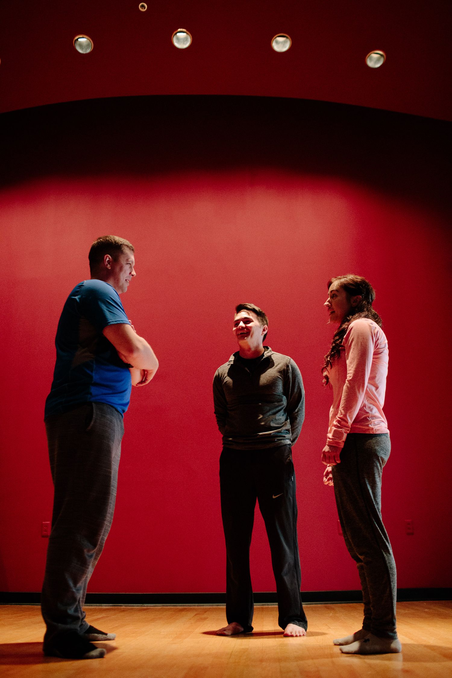 Three people stand in silhouette against a red wall during a performance or rehearsal.