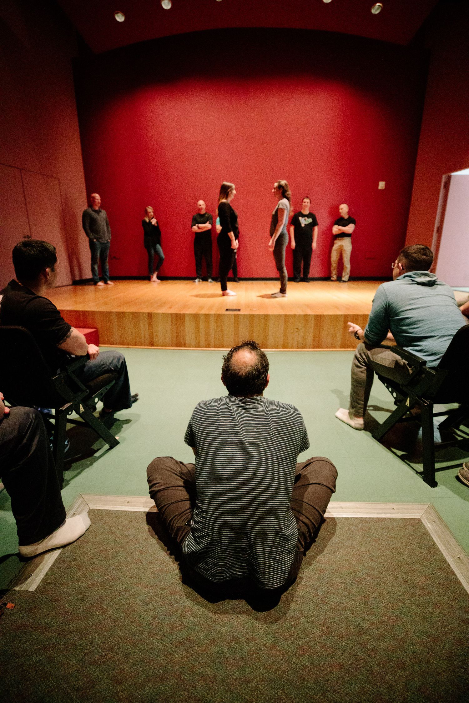 People watching a performance or demonstration in a room with red walls and dark carpeting.