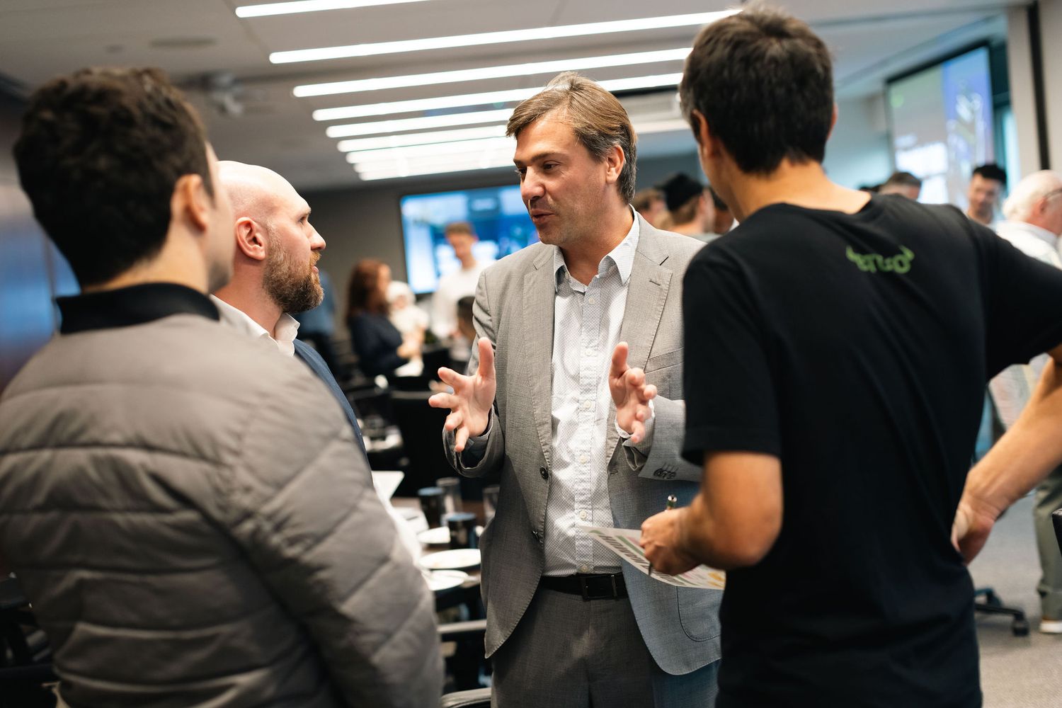 Business professionals engaged in animated conversation during a networking event in an office hallway.