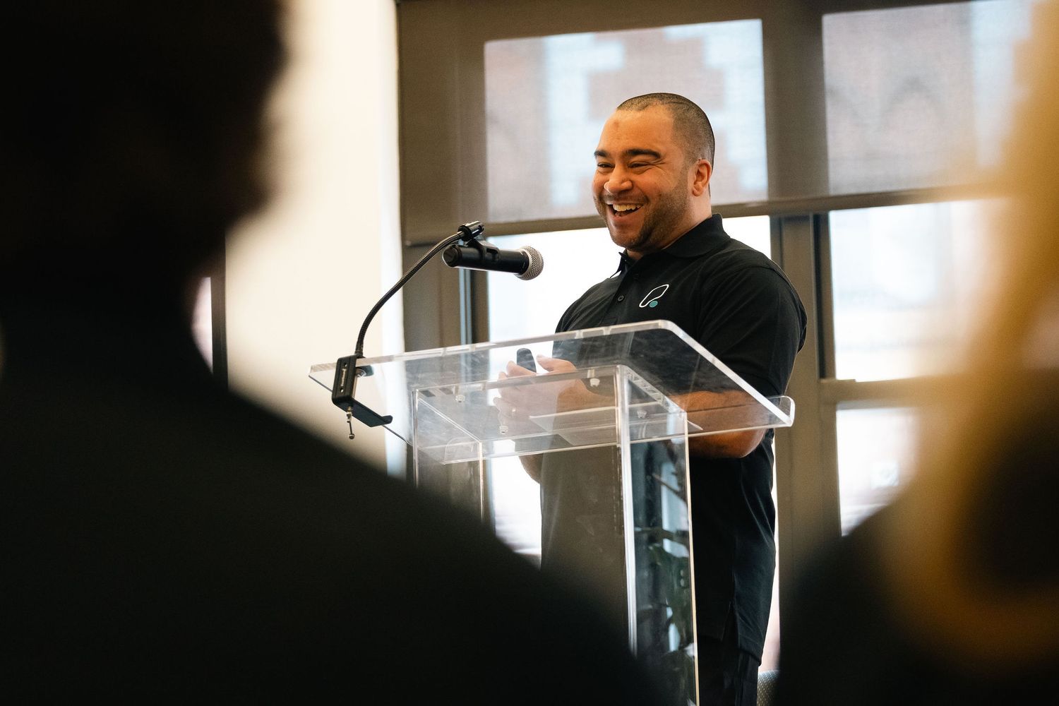A speaker stands at a clear acrylic podium while delivering remarks during an event.