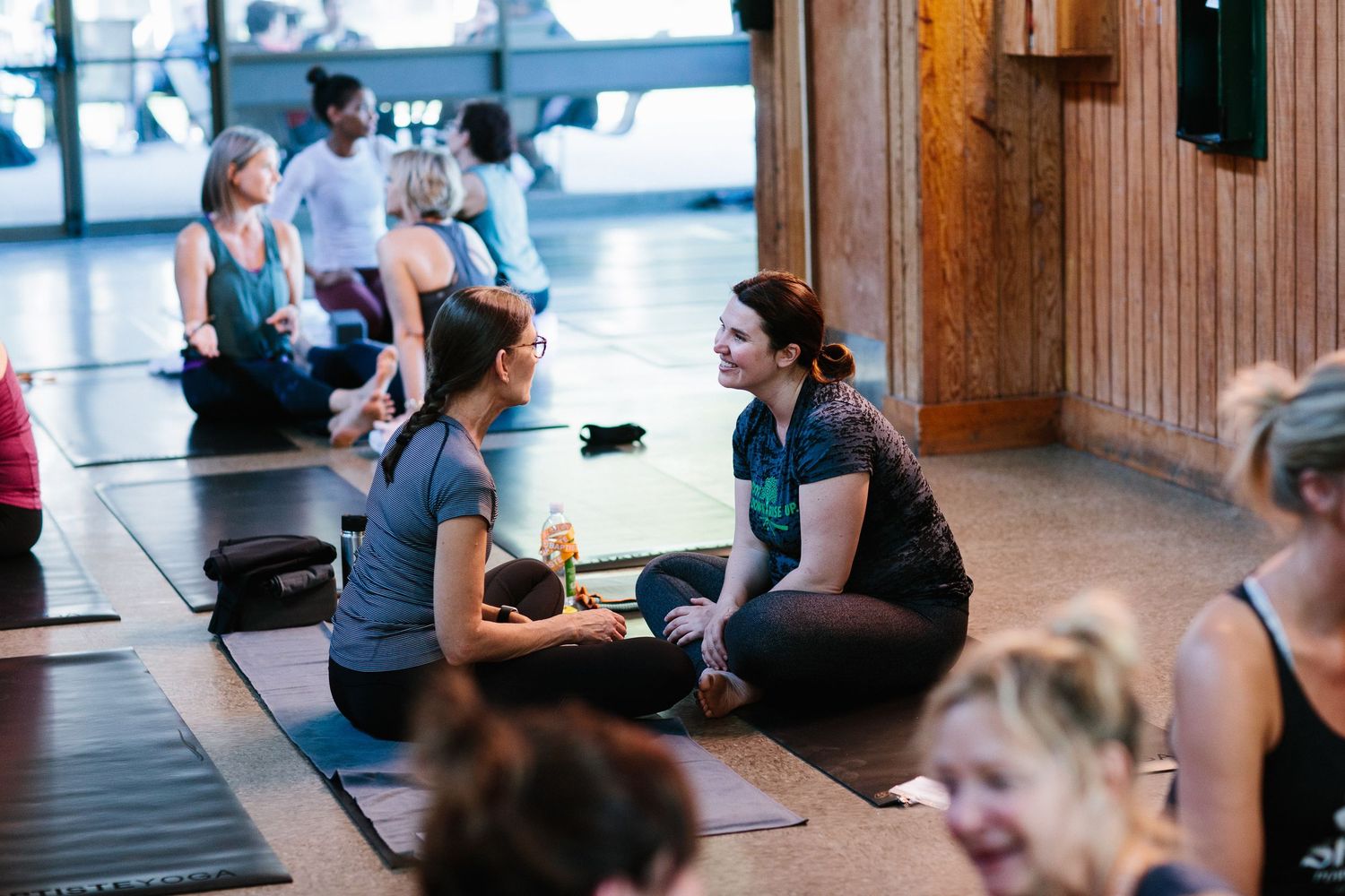 People in athletic wear practicing yoga and meditation in a rustic wooden studio space.