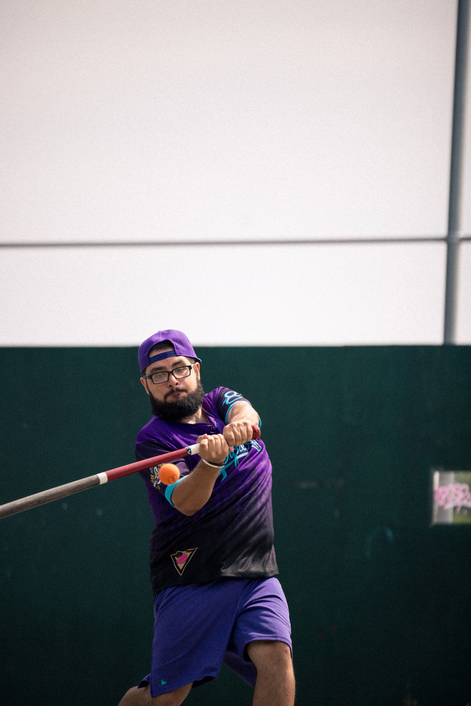 Baseball player in purple uniform and cap swings a bat during indoor practice session.