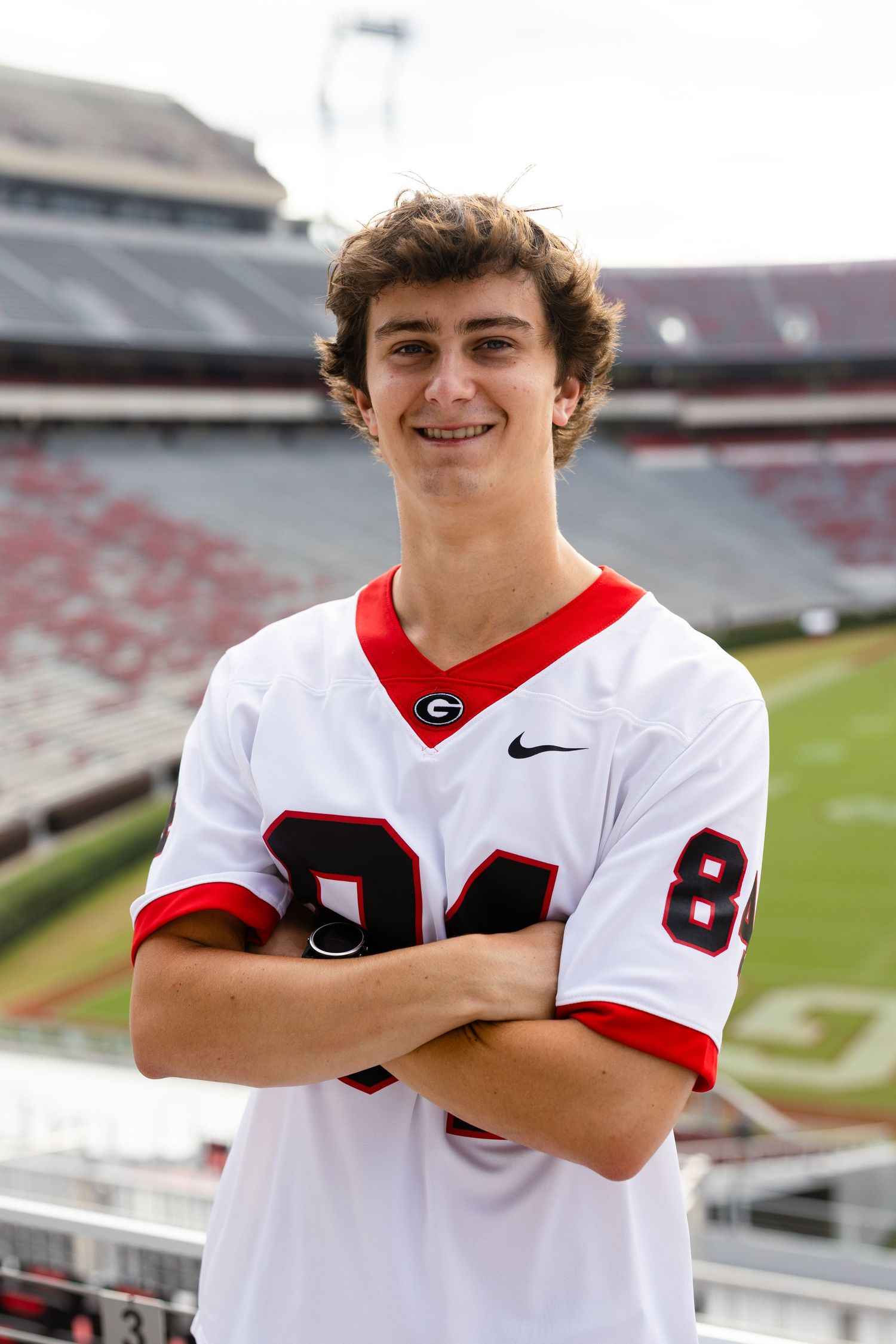 Student athlete poses in white and red uniform at football stadium.