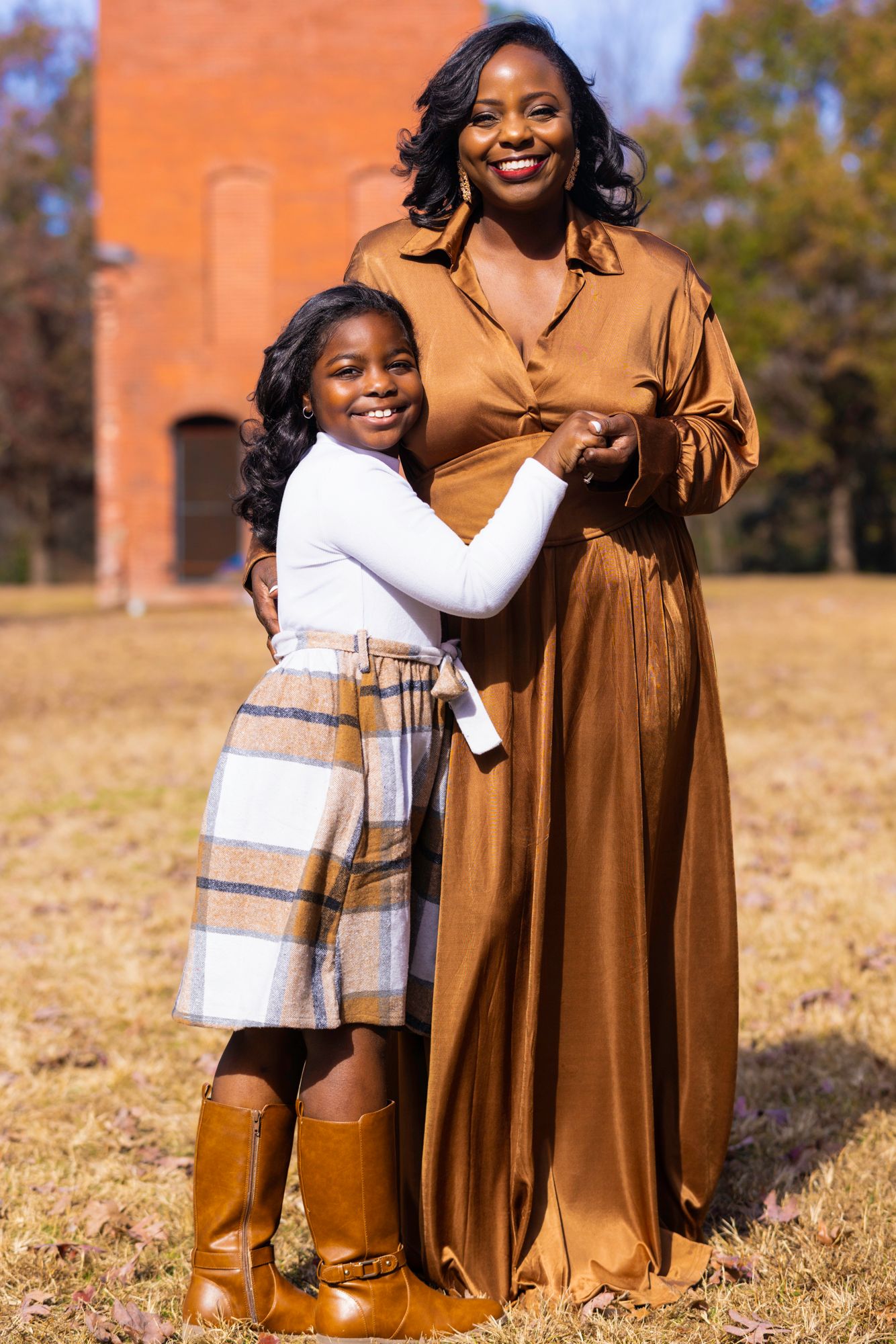Family wearing coordinated brown and white outfits pose together on grassy hill.