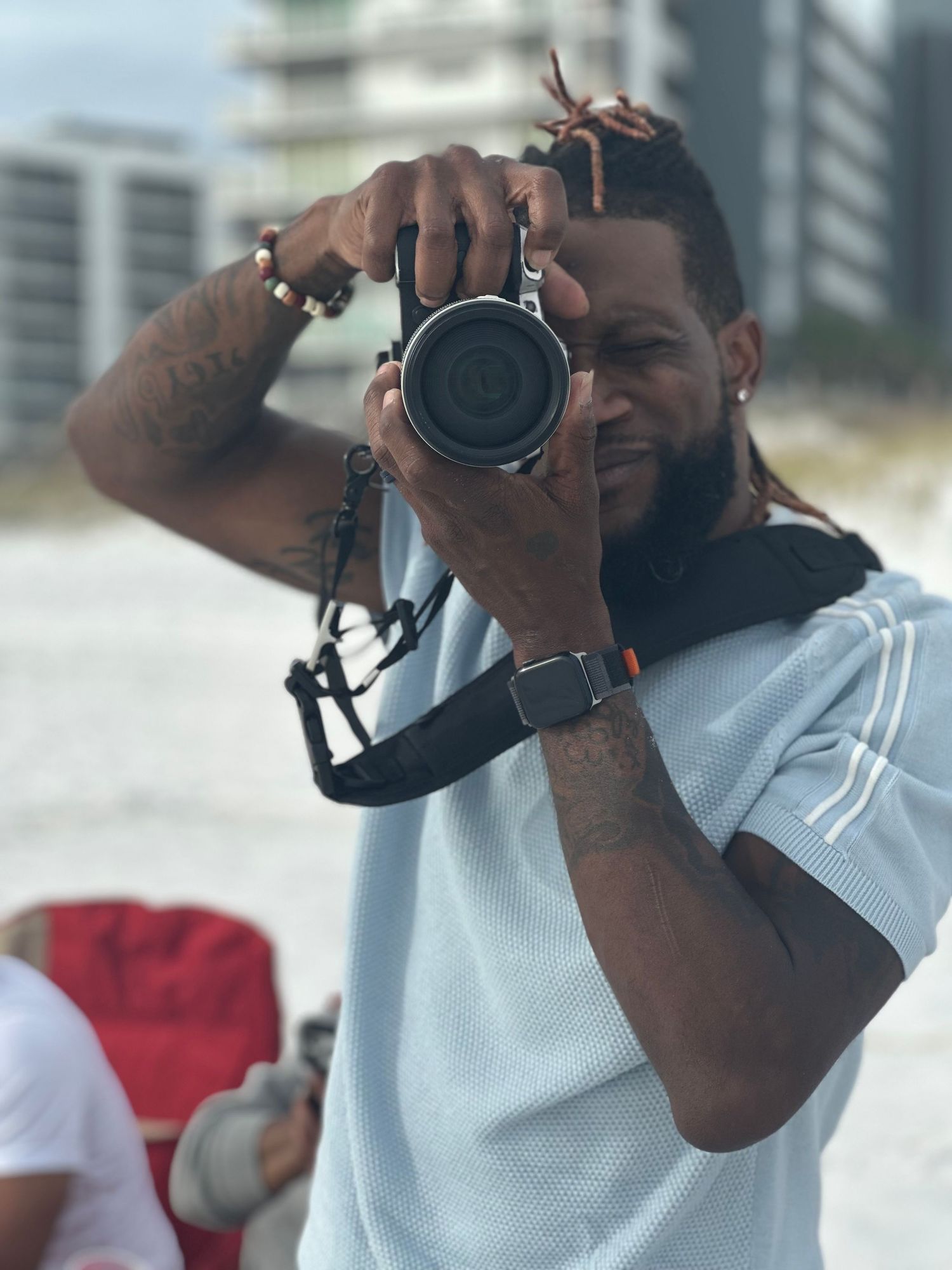 Professional photographer holding a DSLR camera with a lens against an urban background.