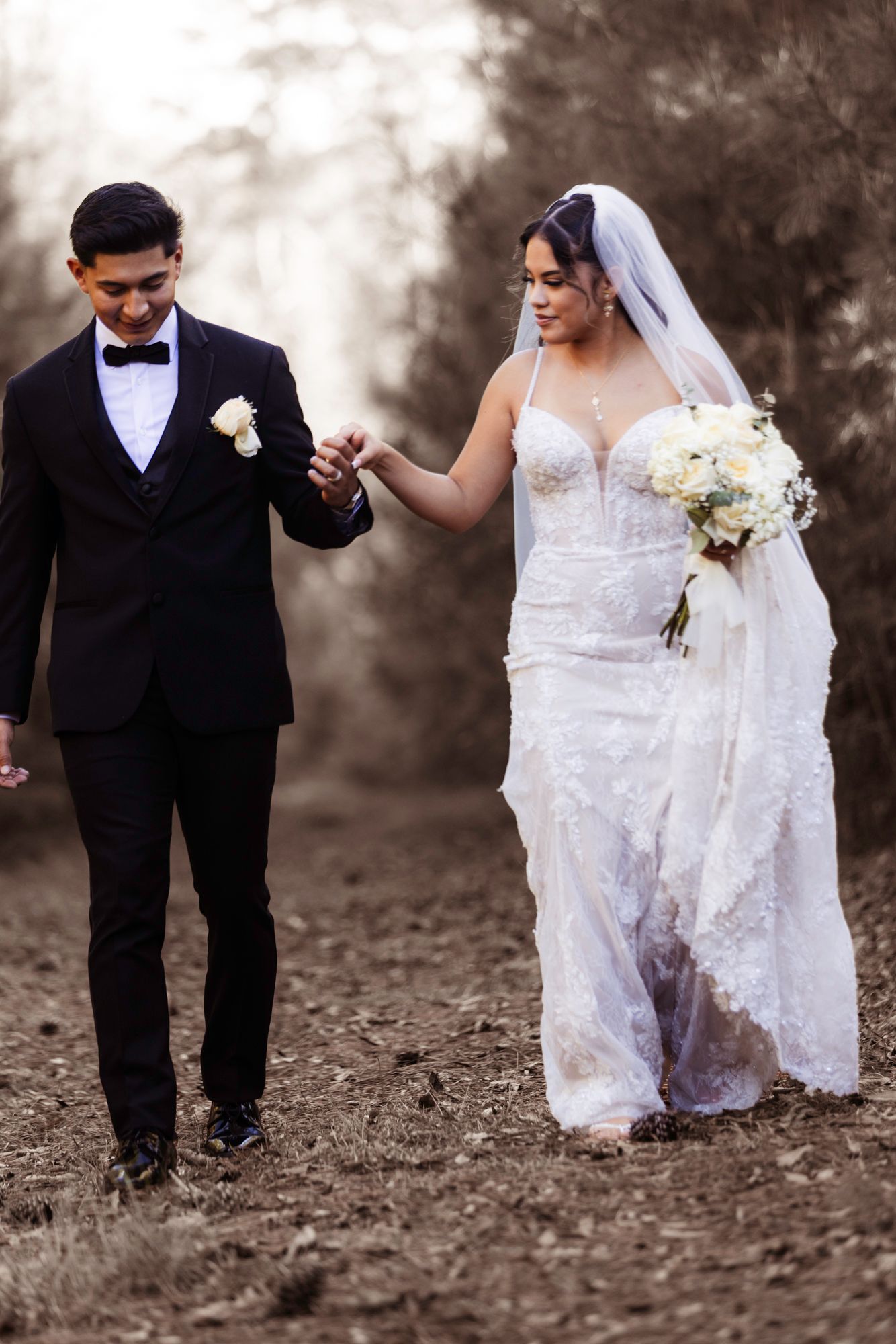 Sepia-toned wedding photo of couple walking hand in hand on a rustic path.