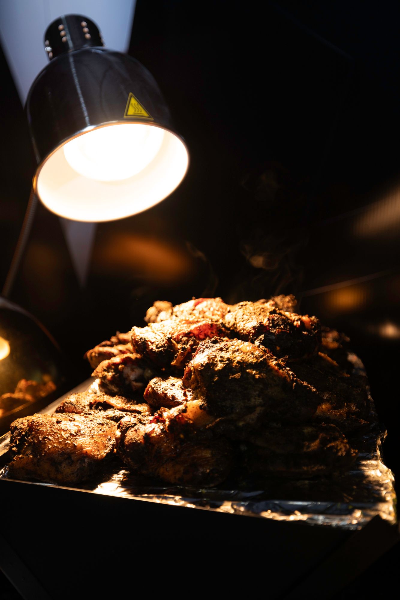 Grilled meat cooking under pendant lighting in a dark setting creates dramatic shadows and highlights.