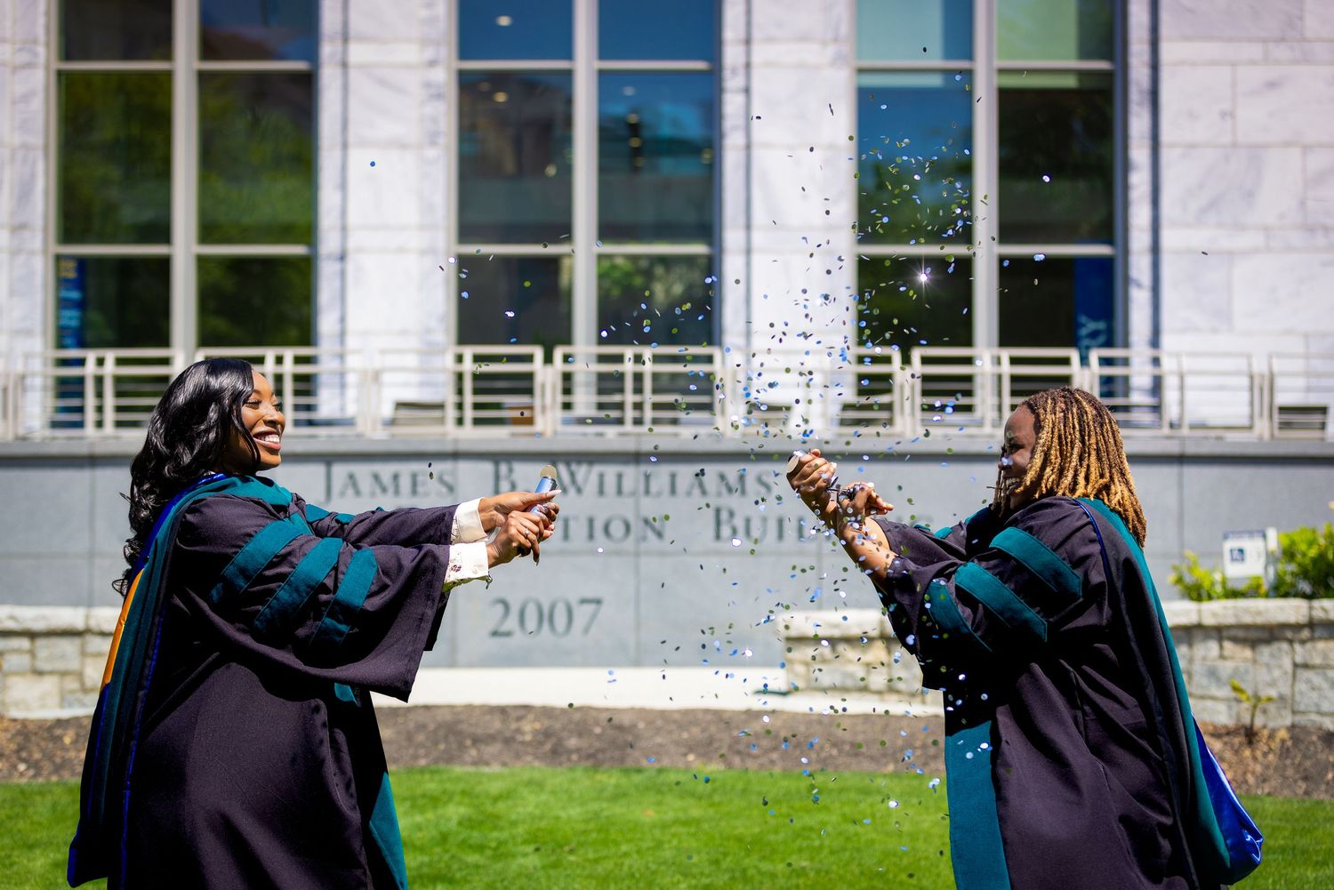 Graduate in academic regalia celebrates on campus with joyful poses against building exterior.