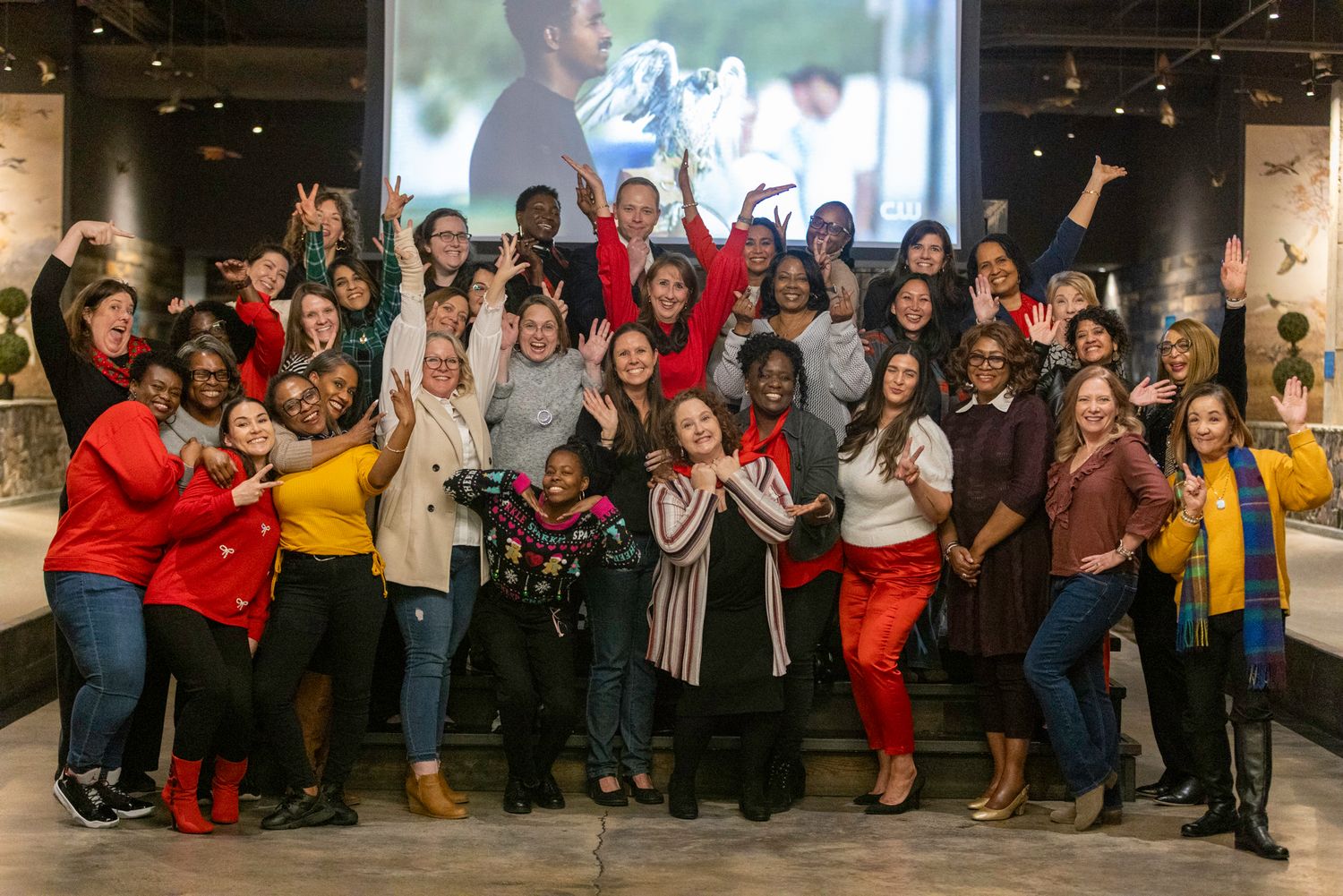 Large diverse group poses together for celebratory photo in front of projection screen.