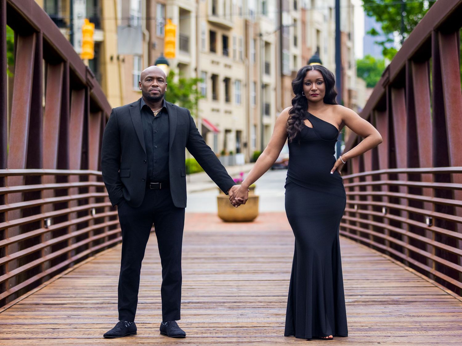 A couple poses on a wooden bridge in formal black attire during their engagement session.