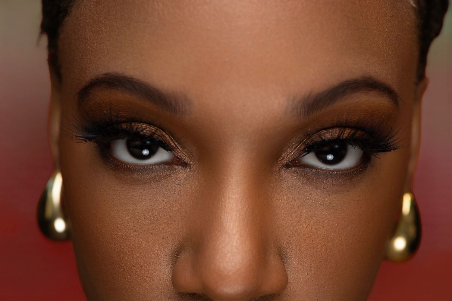Close-up beauty portrait highlighting dramatic eye makeup and gold earrings.