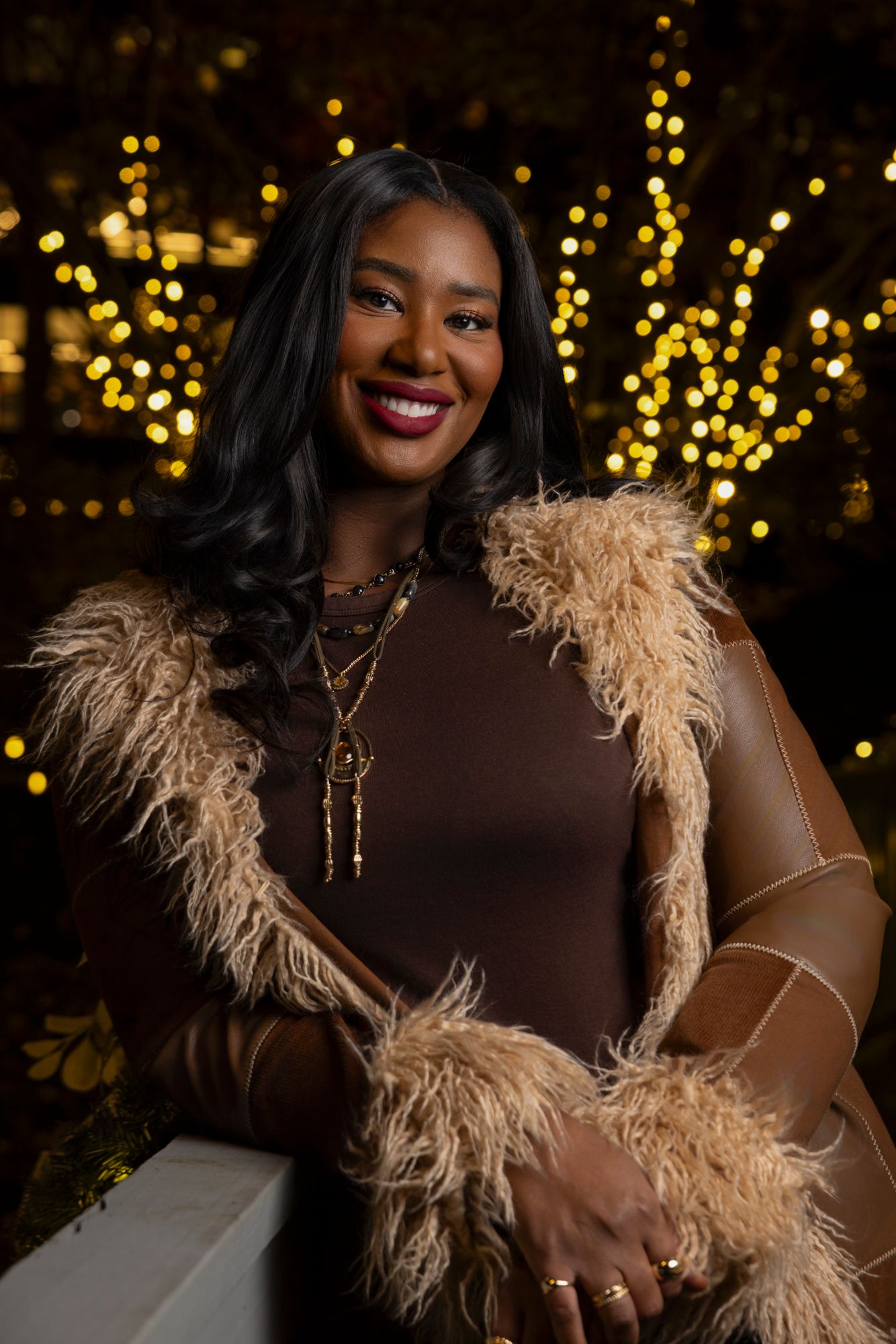Glamorous portrait with feather boa against dark background with golden bokeh lights.