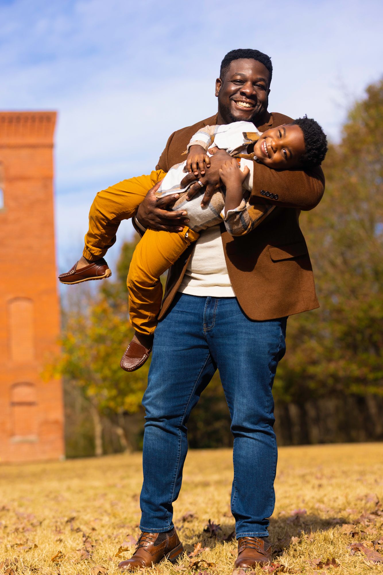 Playful couple in brown and white outfits pose together in autumn field.
