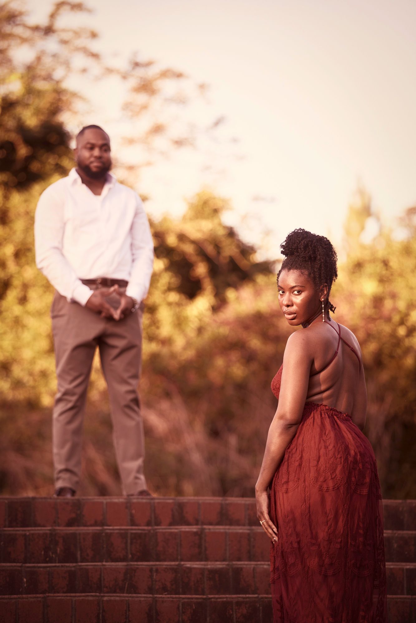 A romantic sunset photoshoot on brick steps with a person in a burgundy dress and another in casual attire.