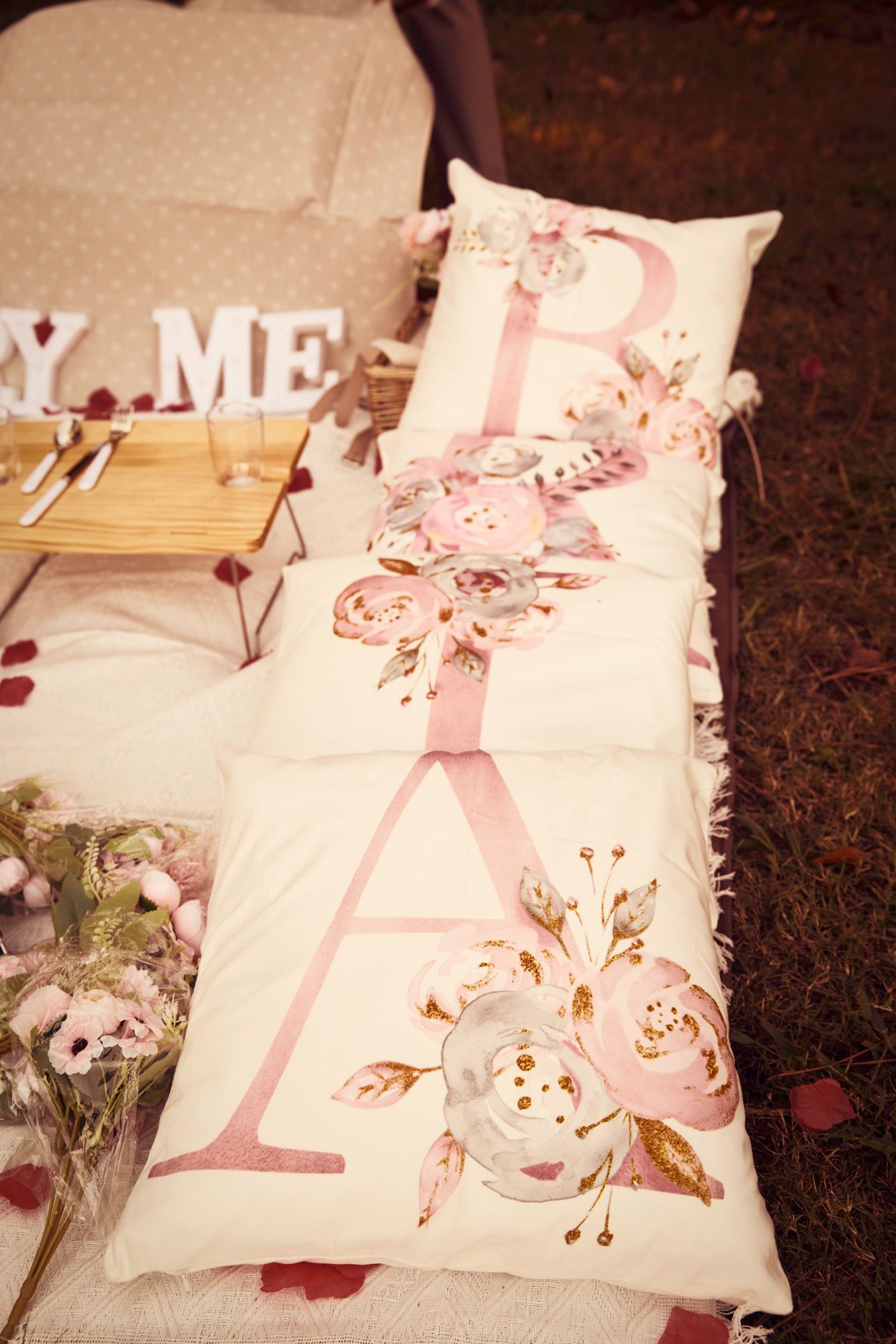 White decorative pillows with 'MARRY ME' text surrounded by rose petals.