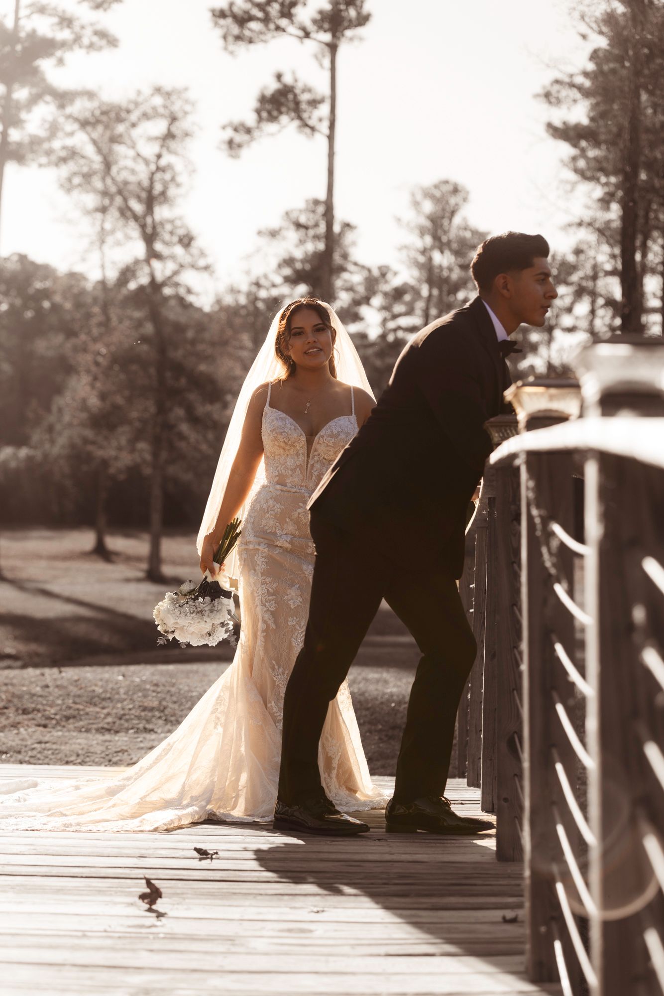 A vintage-style wedding photo capturing a couple in dramatic lighting on a wooden walkway.
